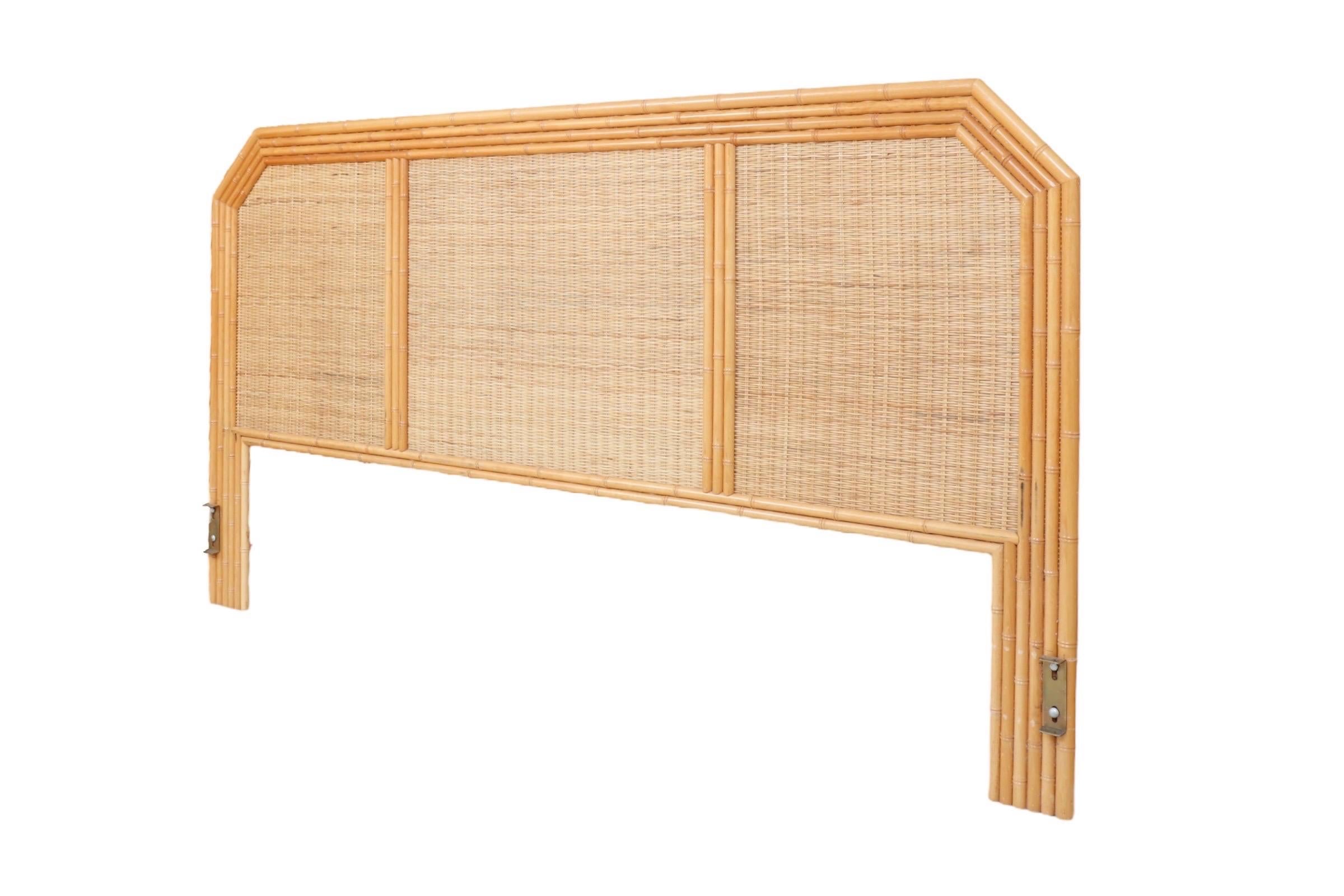 A bamboo and wicker king size headboard. A border of split bamboo frames the wicker headboard into three panels. Legs have metal fittings to attach to a bed frame.