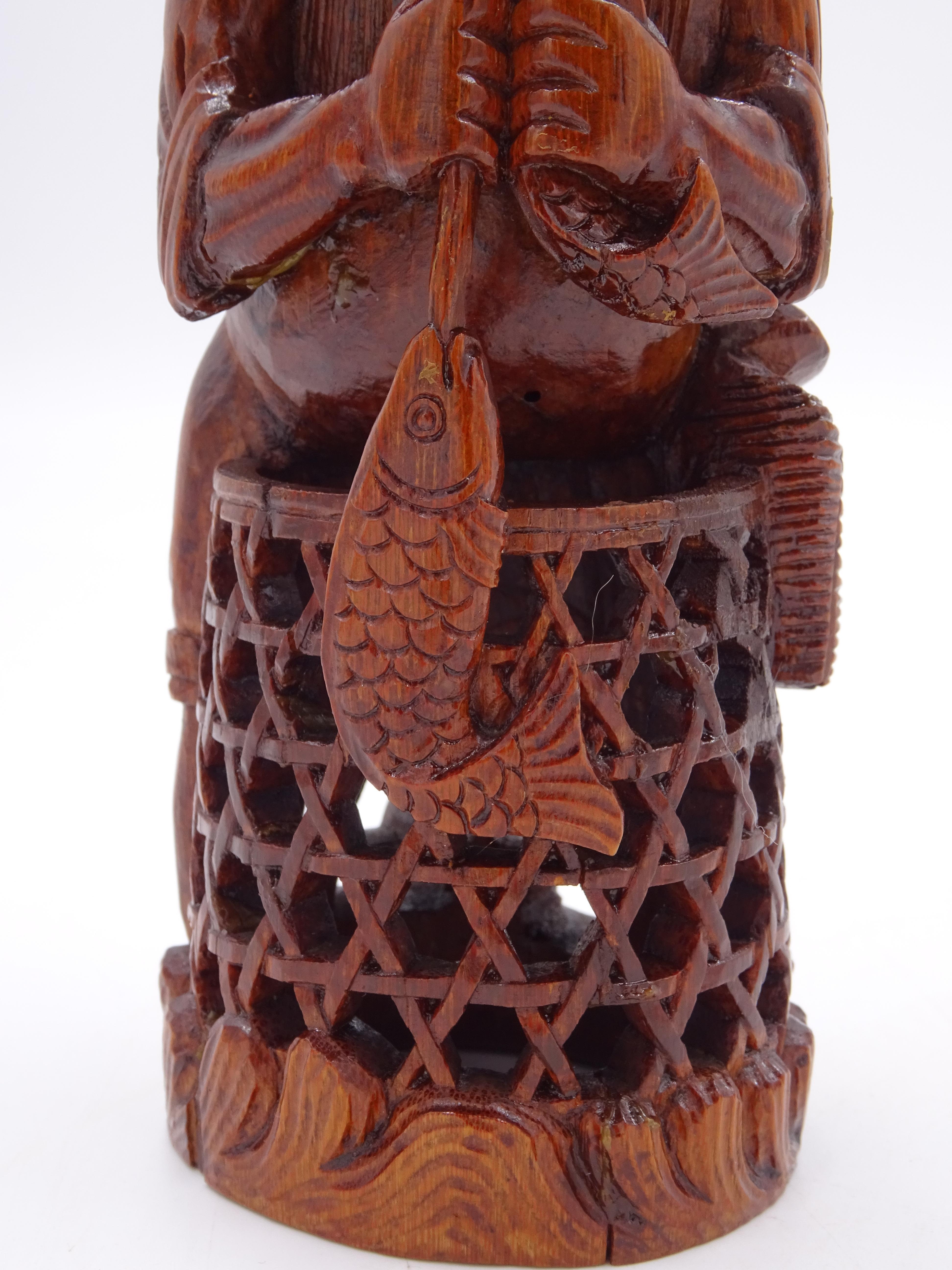 Bamboo wood sculpture depicting a fisherman with oriental features, with a long beard and wearing a headdress, while holding two fish in his hand.

The lower part is embellished with an elaborate carved fishing net. 
The work is of Chinese