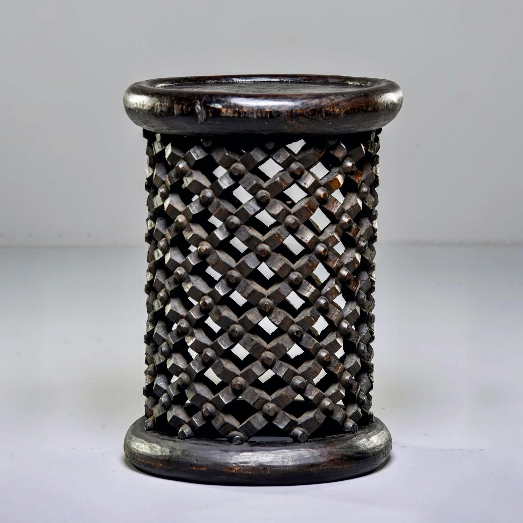 This circa 1980s hand carved narrow pedestal style stool or side table was made from a single piece of wood by the Bamileke people of Cameroon. The intricate knobby carved lattice work of the base symbolizes life’s webs that bind us together. Sold