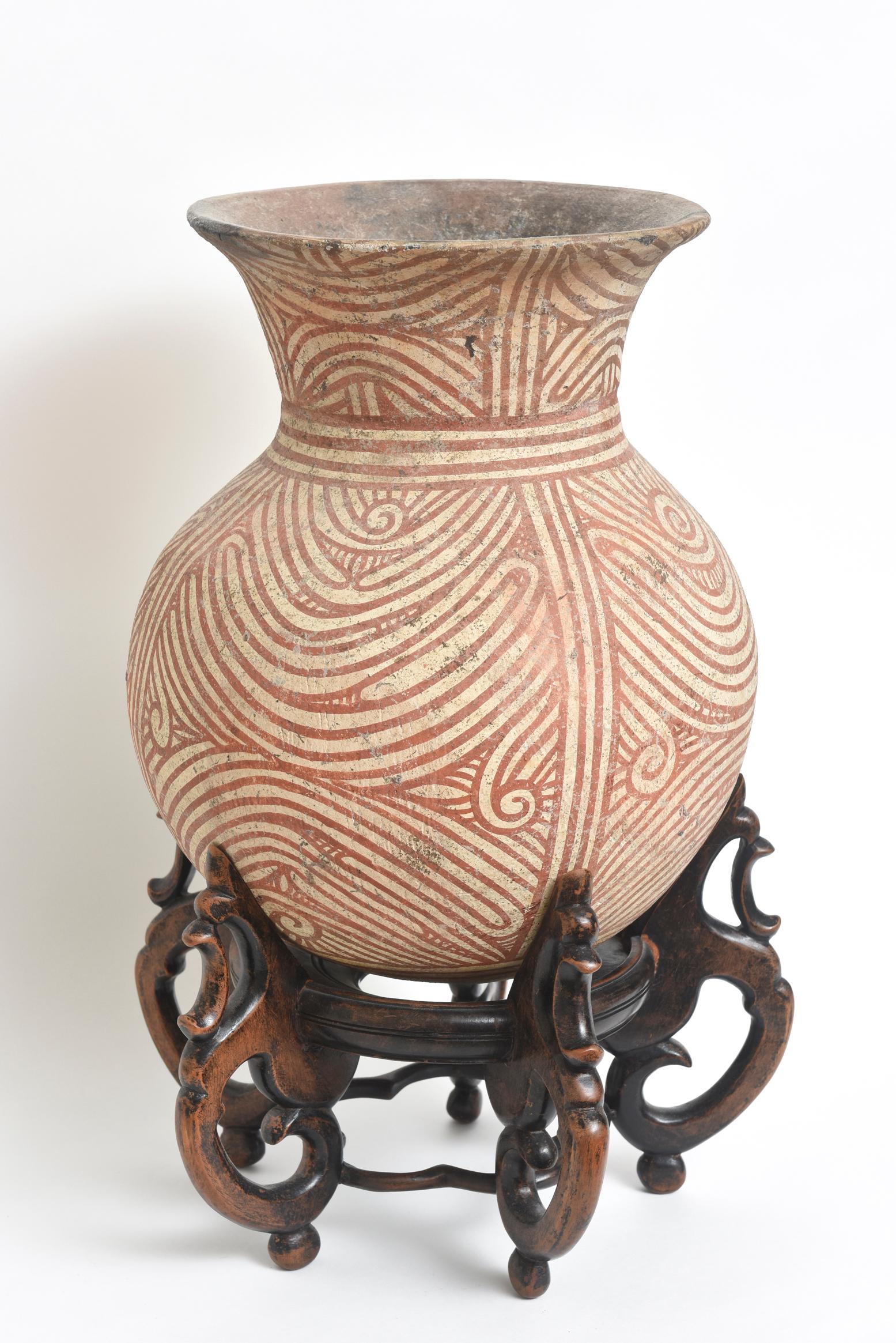 Ancient pottery vessel with a wide body and flared rim. The decoration is done by hand in a darker terra cotta color.
