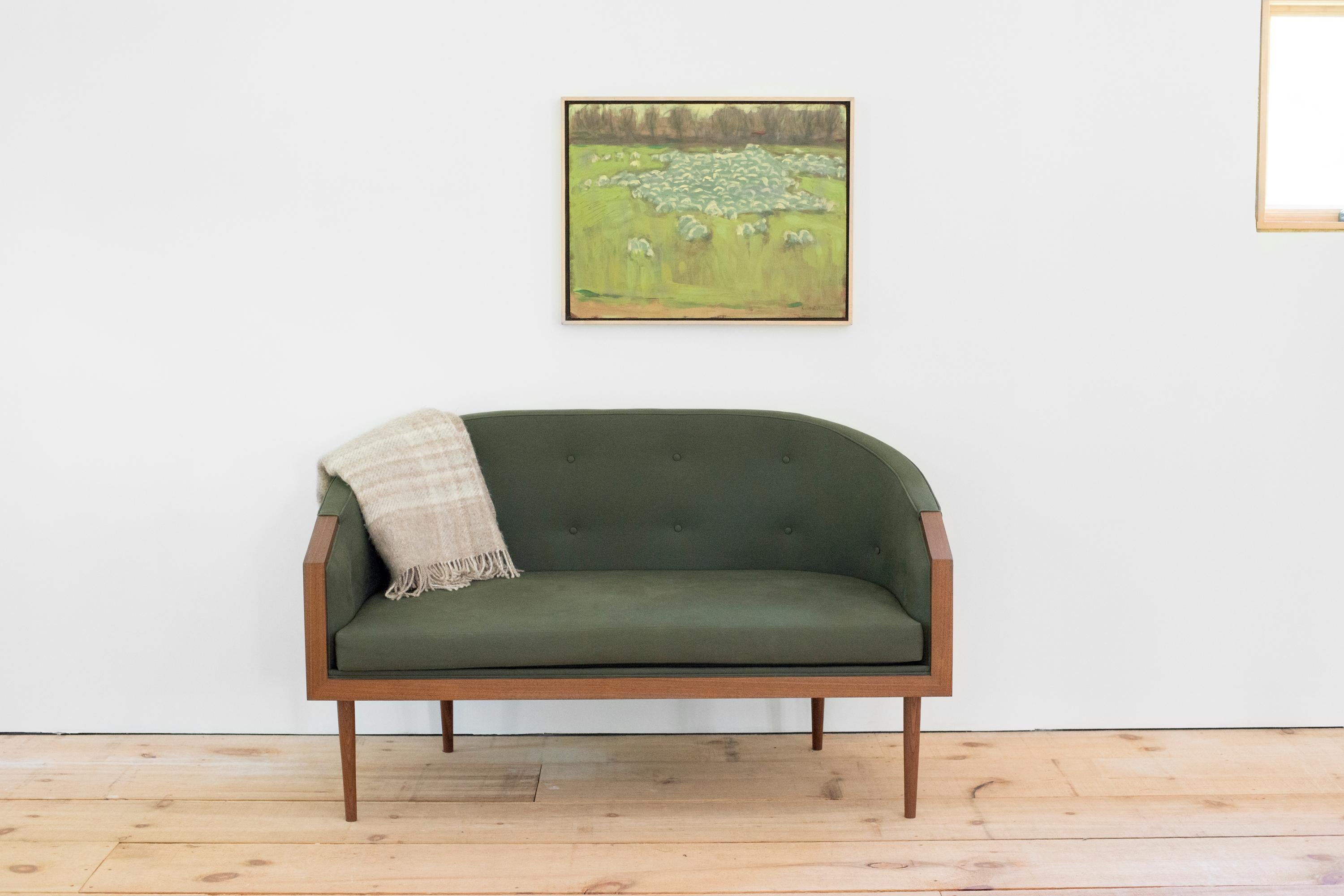 A new iteration which echoes that of our chairs of the same name, the loveseat, shown here in walnut with green cotton upholstery and two rows of button tufting, uses an elongated barrel form to cradle the body. Four hand-turned and tapered legs