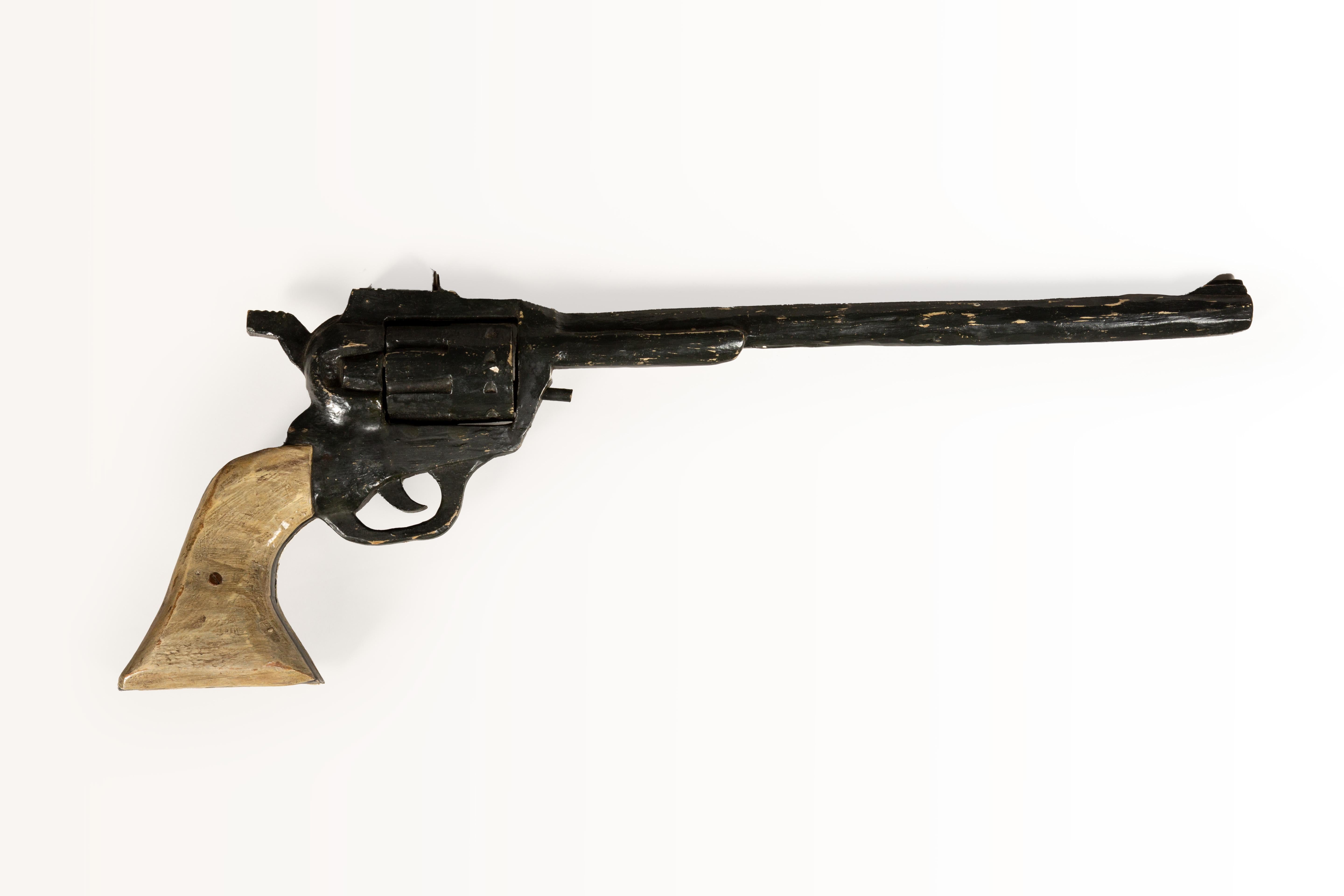 This unique carved wood revolver trade sign features a stylized depiction of a classic six-shooter pistol, meticulously handcrafted with a charmingly rustic appeal. Likely used as an advertisement for a gunsmith, general store, or Western-themed