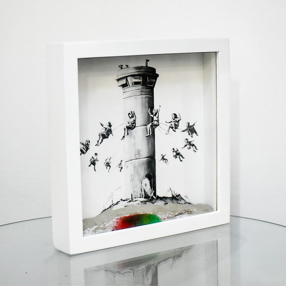 Caja del Hotel Amurallado Banksy.
La impresión muestra la misma obra de arte que Banksy pintó originalmente en el muro de separación de Jerusalén.
Grabado que representa las torres de vigilancia del muro de separación convertidas en un columpio.
El