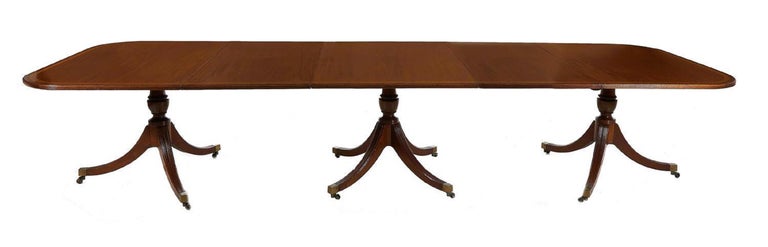 Banquet Size Georgian Style Inlaid Mahogany Triple-Pedestal dining table inlaid top, reeded baluster pedestal, splayed legs on brass casters; fitted with two 24-inch leaves; Full size dimensions: H28 1/2