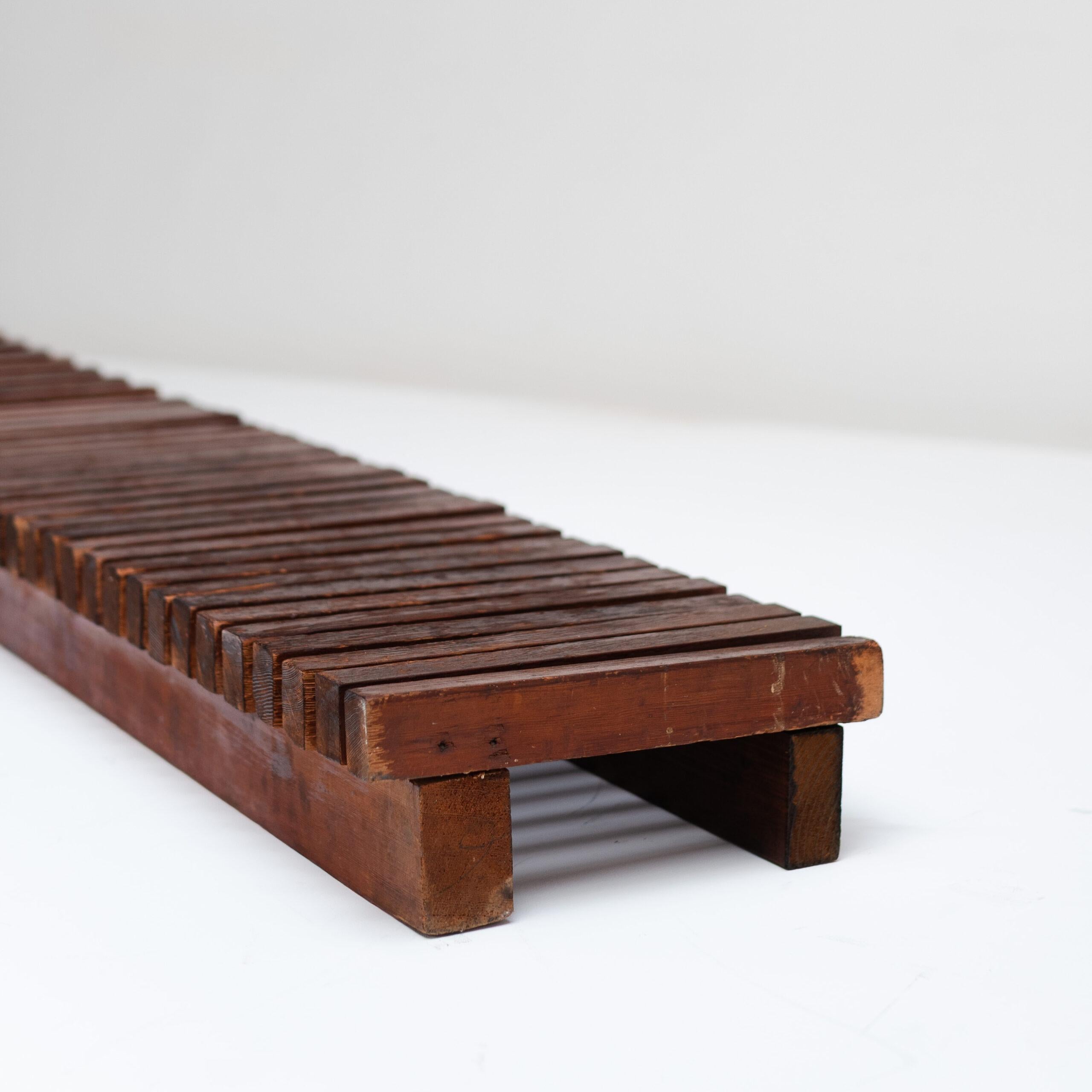 Banc bas (banquette intégrée) conçu par Charlotte Perriand pour la station de ski des Arcs. Sa séquence de lamelles parallèles capture le rythme architectural et la chaleur naturelle qui définissent le modernisme alpin de Parallele.