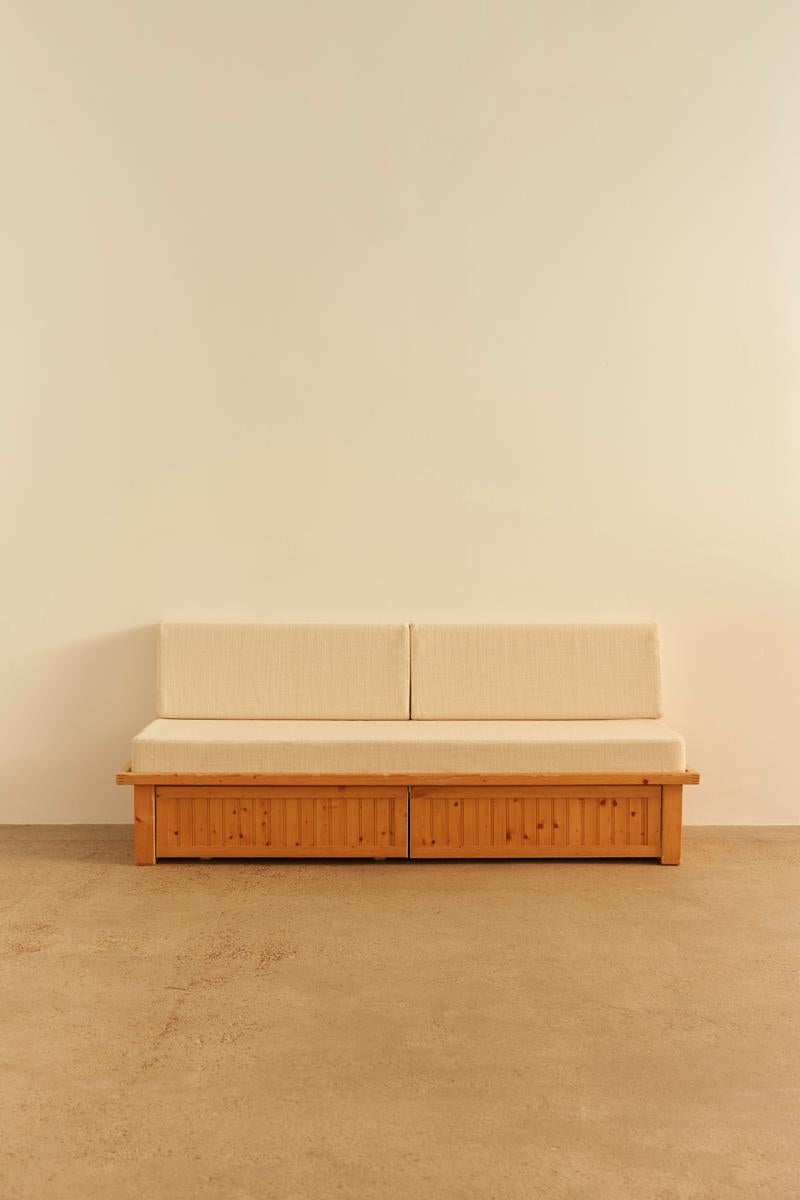 Originalmente parte de la emblemática Résidence Nova de Les Arcs, diseñada por Charlotte Perriand, este sofá cama presenta una estructura de listones de pino con discretos cajones rodantes ocultos tras un frente abatible. El colchón del asiento y