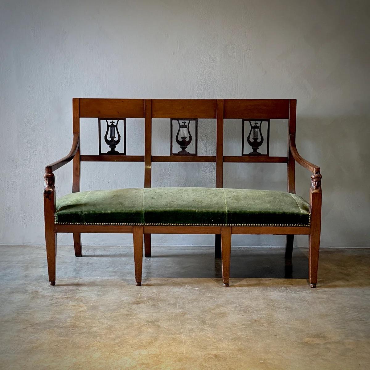 Esta banqueta o canapé Imperio encarna la elegancia clásica y la refinada artesanía de la época. Fabricada en rica madera de frutal, esta pieza presenta un elegante asiento tapizado que realza su lujoso atractivo. Su nobleza se debe a su estructura