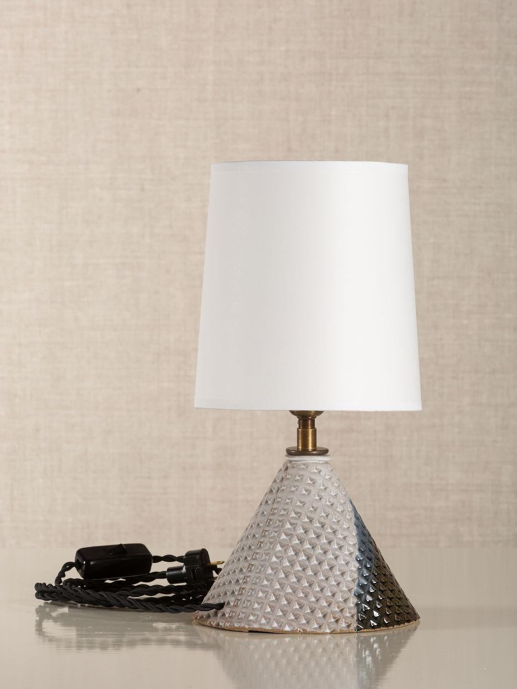 Description:

Handmade stoneware slab construction. Lamps are individually crafted and one of a kind.

Finish:

Parchment & bottle green glaze. Antique brass fittings with braided black cloth cord. Available with off-white paper or linen clip