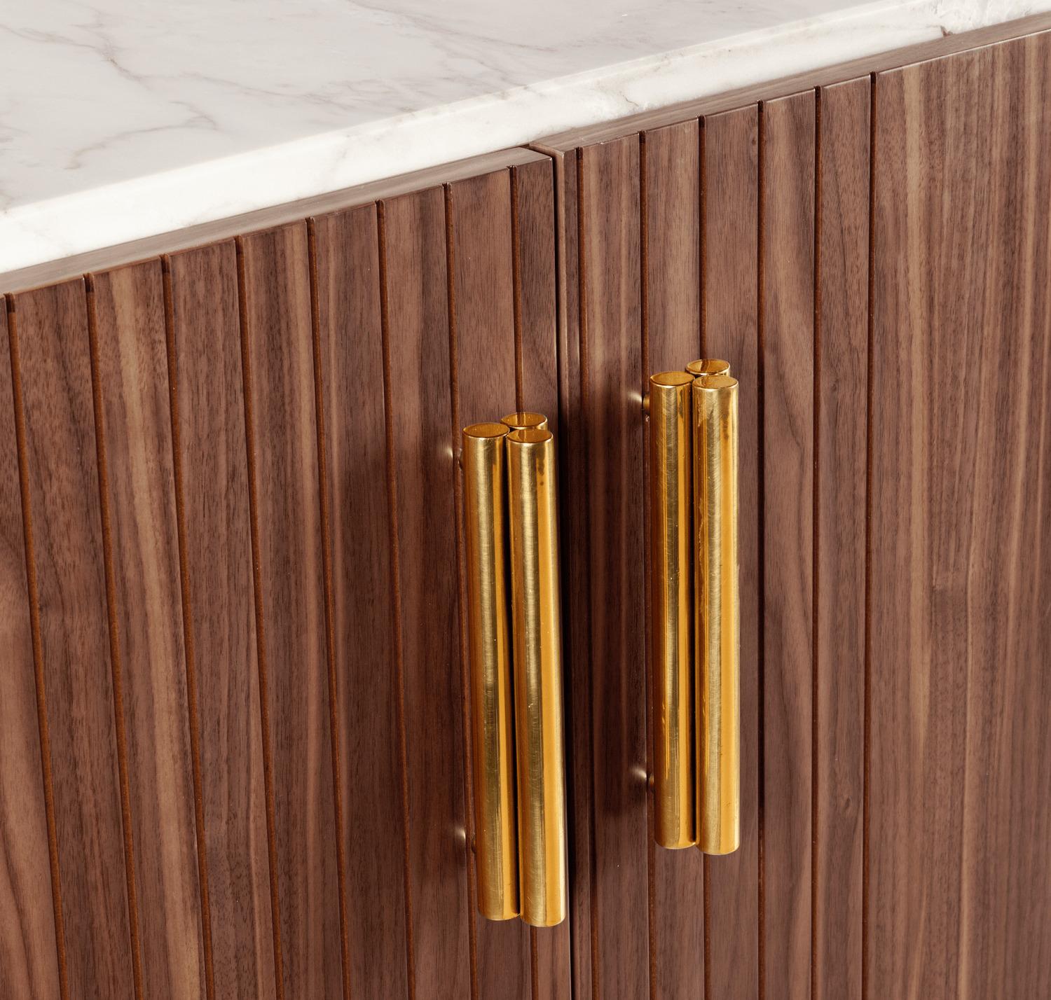 Malcolm bar cabinet is a high quality product by Mambo Unlimited Ideas, crafted in carved wood veneer, brass applications and a marble top. It features slanted corners, elegant polished brass handles, discreet brass feet, and a wood veneer body,