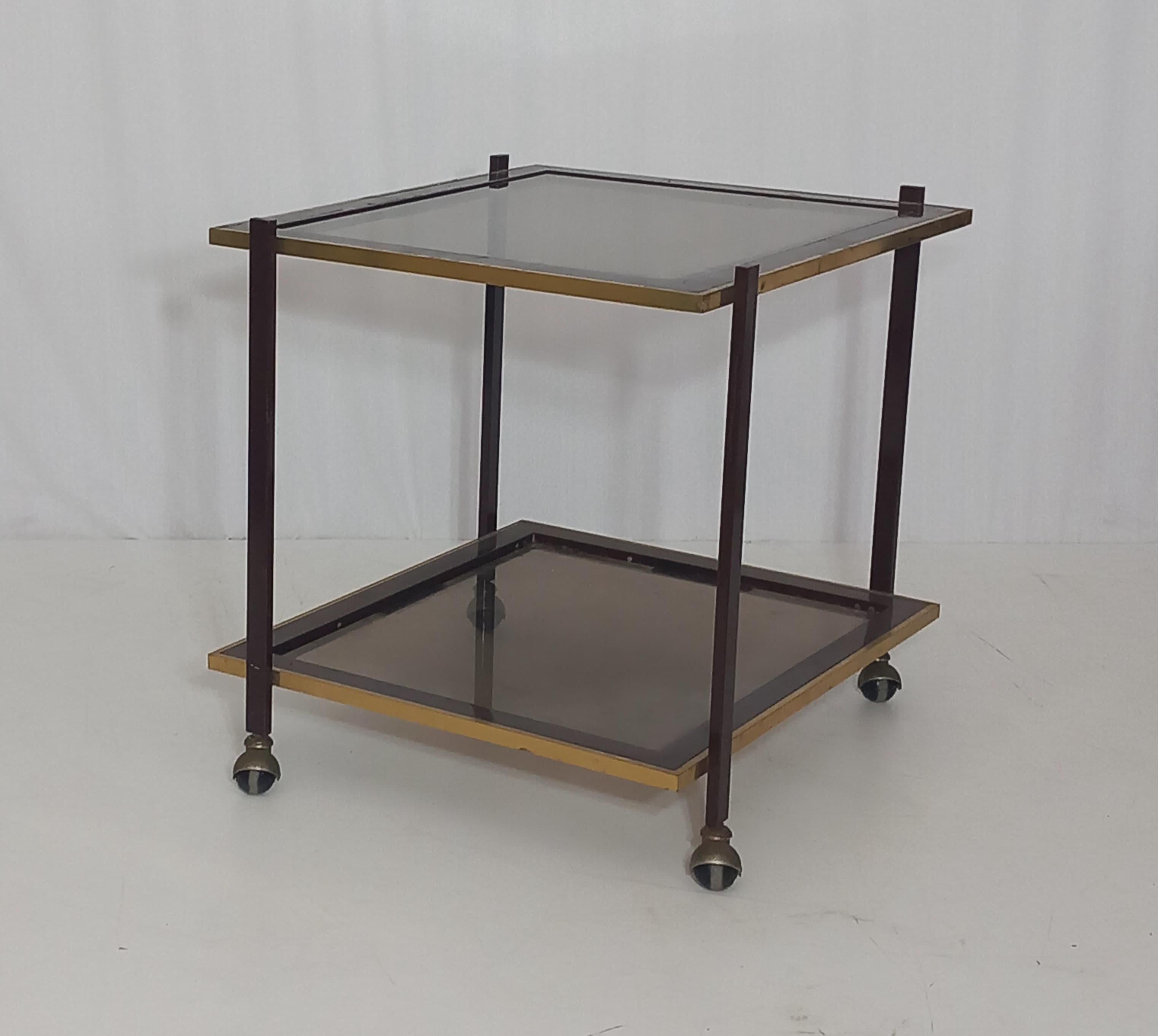 Introducing a mid-century bar cart displaying the iconic design aesthetics from the 70s. The bar cart structure is made of metal, while the support surfaces of glass. This classic piece adds a touch of elegance to any home decor showcasing