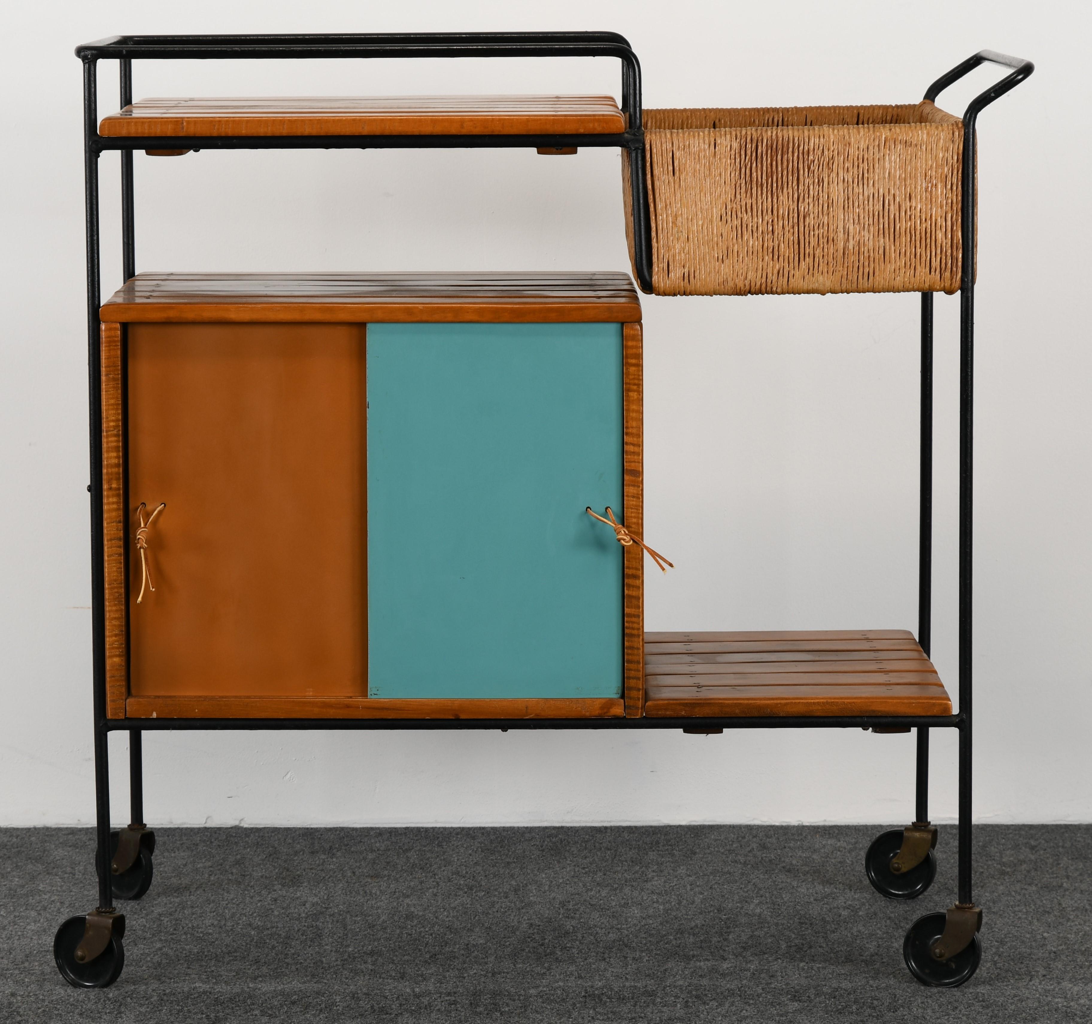 A vintage Mid-Century Modern rolling bar cart made of wrought iron, rope, and leather designed by Arthur Umanoff. This piece is in very good condition and has a rope sectioned carry all with three shelves constructed of maple wood. The doors consist