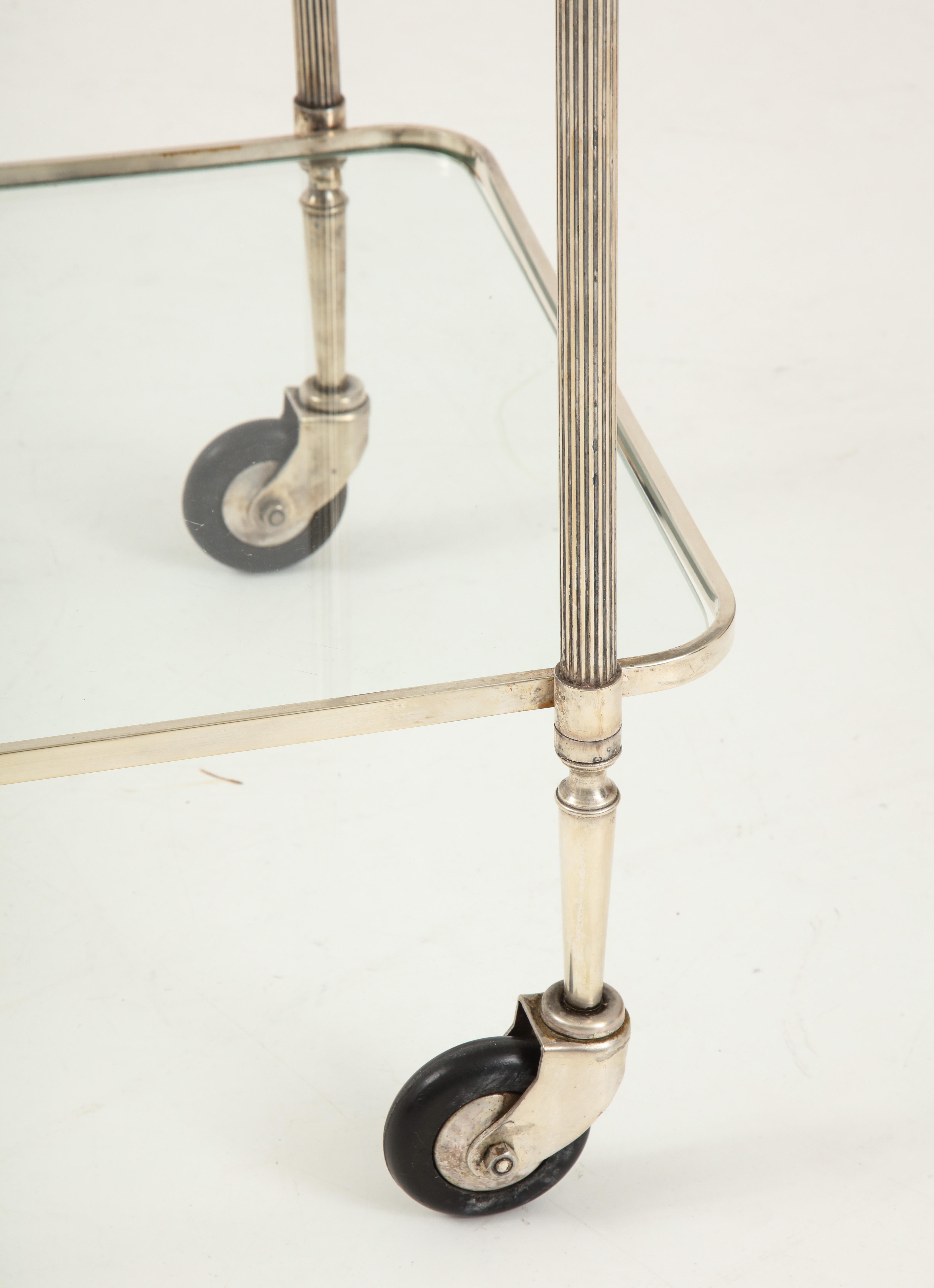 A chic bar cart in polished Nicke with a lower glass shelf and a removable upper tray with a gallery. This gem features lovely details, including reeded legs and handle as well as charming acorn finials. Its size make it quite versatile and useful.