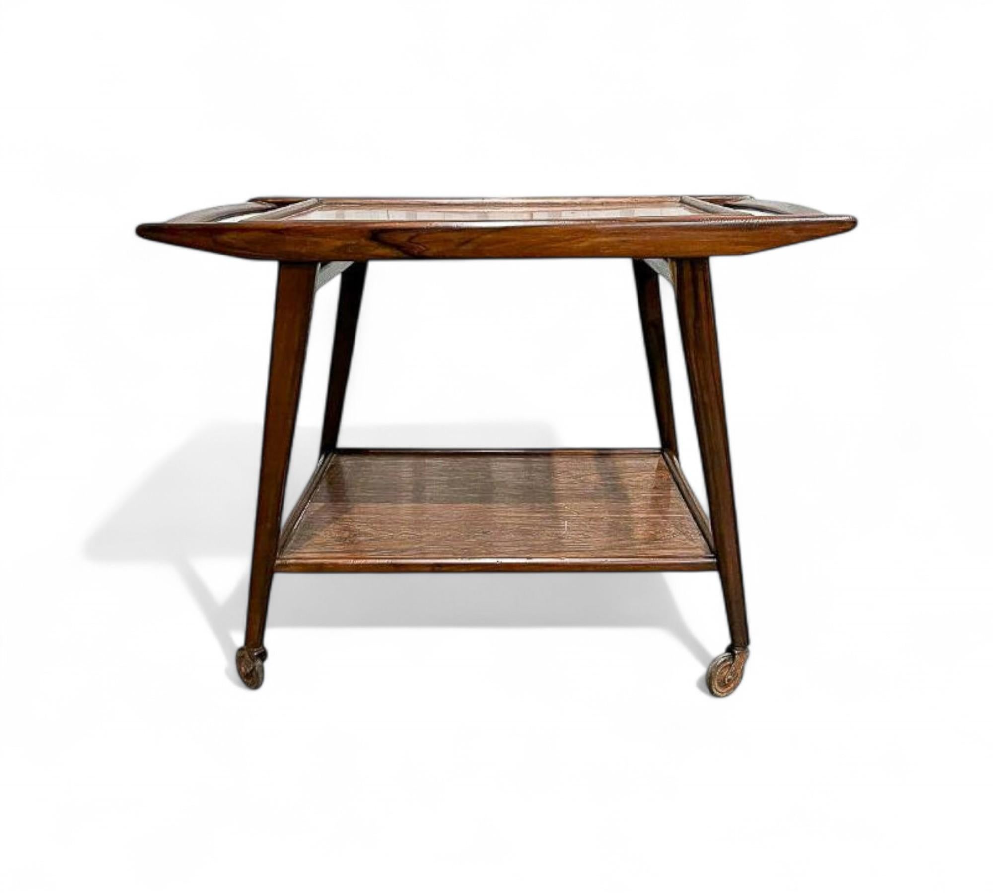 Made in the 1960s, this bar cart, also known as a tea trolley, boasts a solid hardwood structure with two levels covered in brown Formica. The top level includes a movable tray, while the lower level is fixed. It stands on four legs equipped with