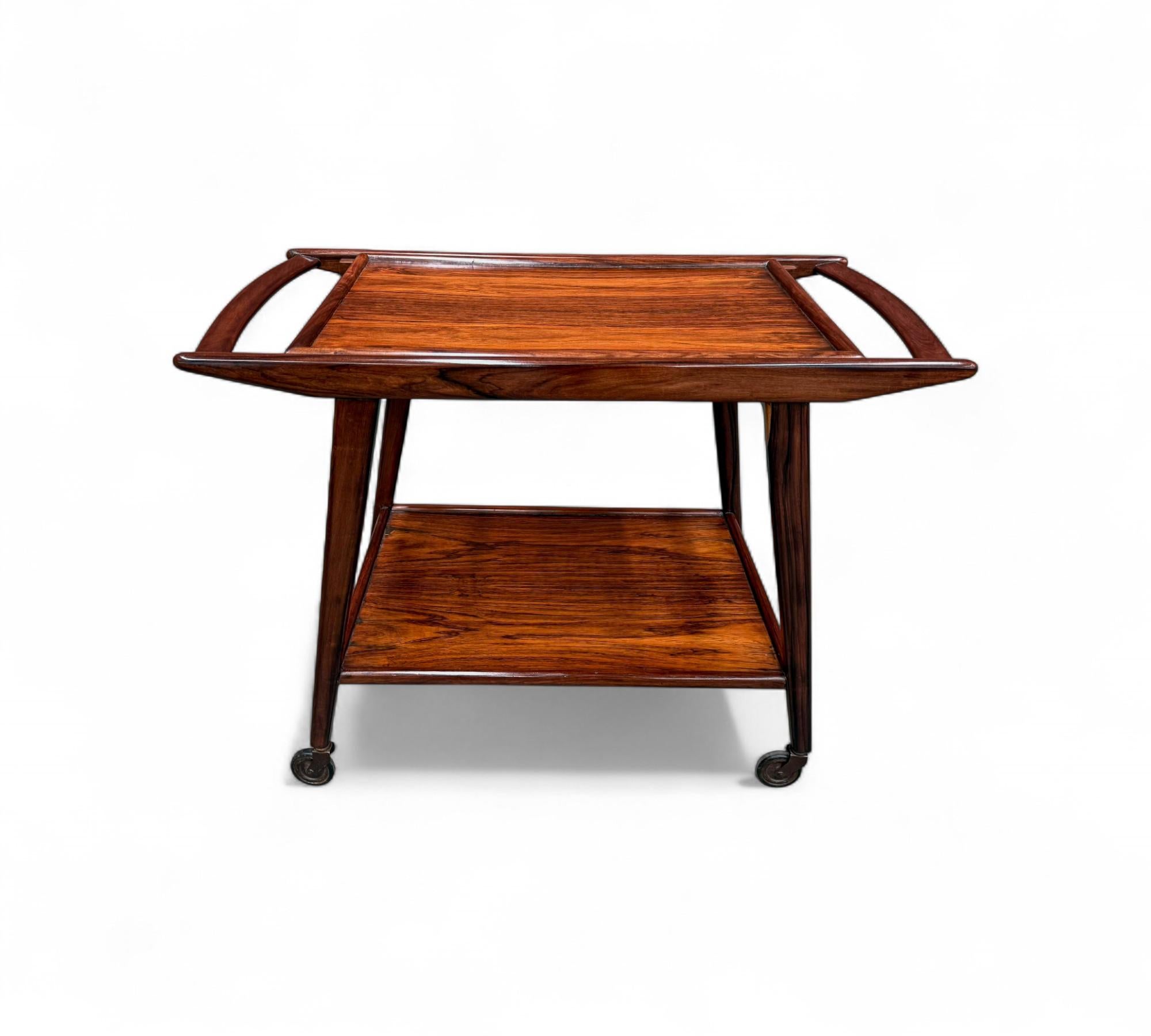 Made in the 1960s, this bar cart—also known as a tea trolley—features a solid rosewood (jacaranda) structure with two levels. The original Formica surfaces were too damaged to be preserved, so they were carefully replaced with high-quality hardwood