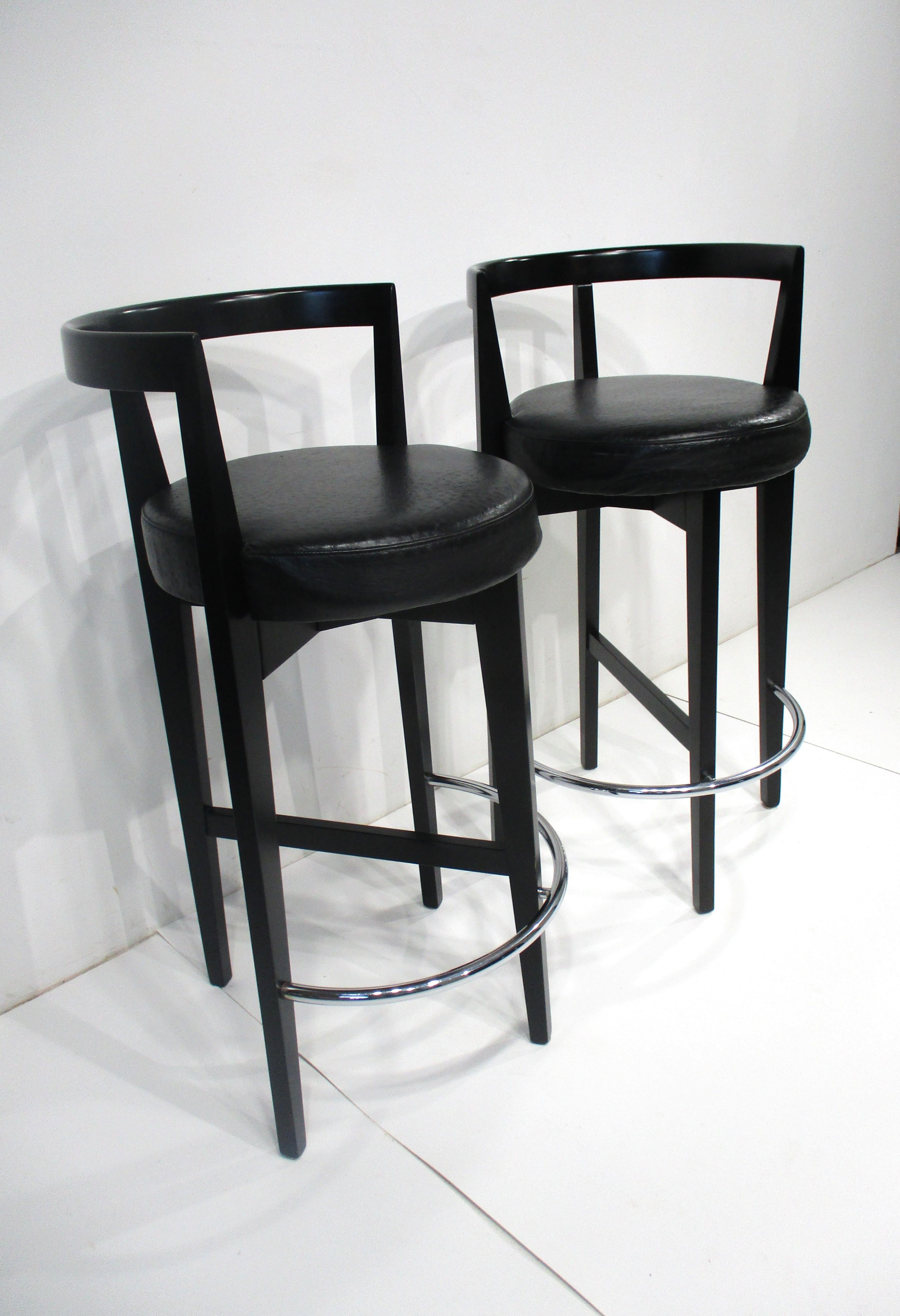 A pair of black wood framed bar / counter stools with ostrich styled leather seats . The rounded backs are great for long periods of comfortable sitting with the legs tapering down to half ring chrome foot rests . Made in Italy in the manner of the