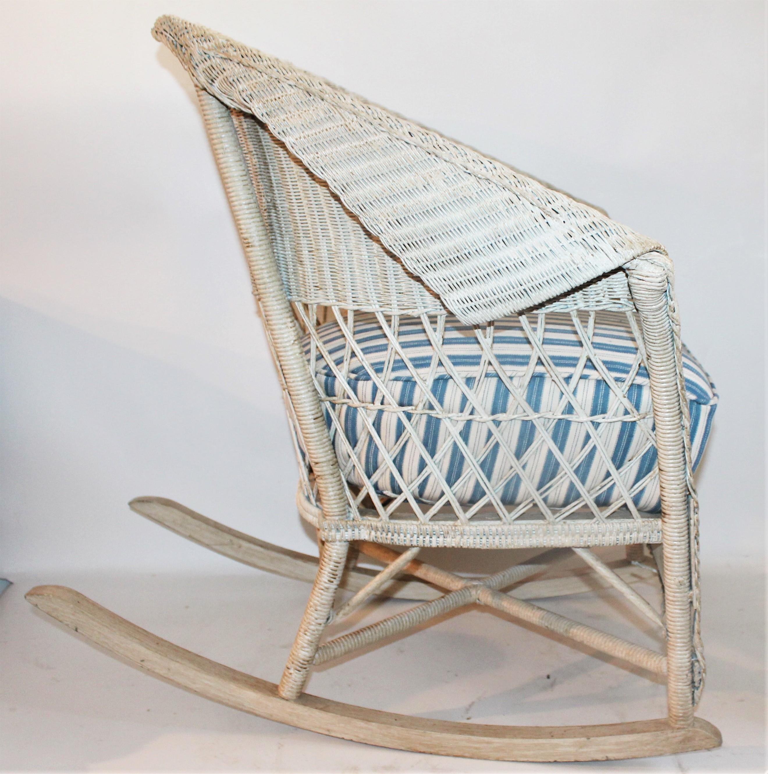 This old cream painted wicker bar Harbor rocking chair is in fine condition with a newly upholstered cushion in vintage ticking. This removable cushion is in fine condition. Very sturdy and comfortable.