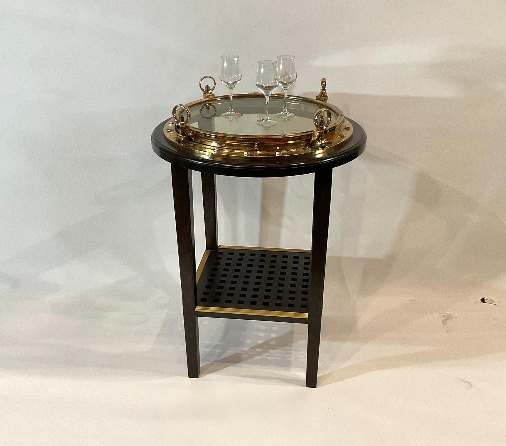 Fabulous bar height porthole table built with an absolutely massive ships porthole. Meticulously polished and lacquered. The porthole top is three feet in diameter. It is mounted into a mahogany table with a ships grating shelf below with brass foot