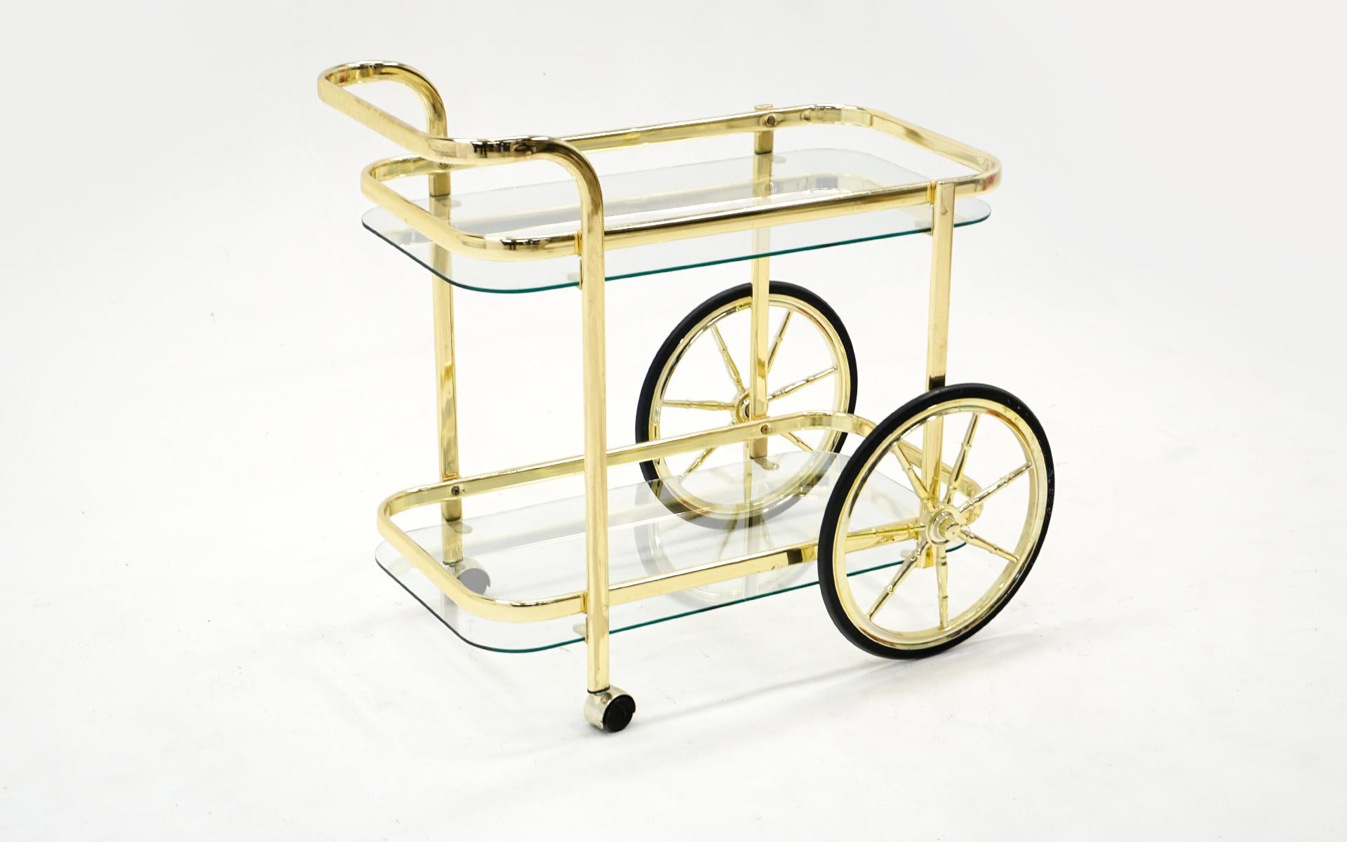 Portable bar / serving cart in brass with two glass shelves and large wheels in very good to excellent condition. Smaller scale. Functions perfectly.