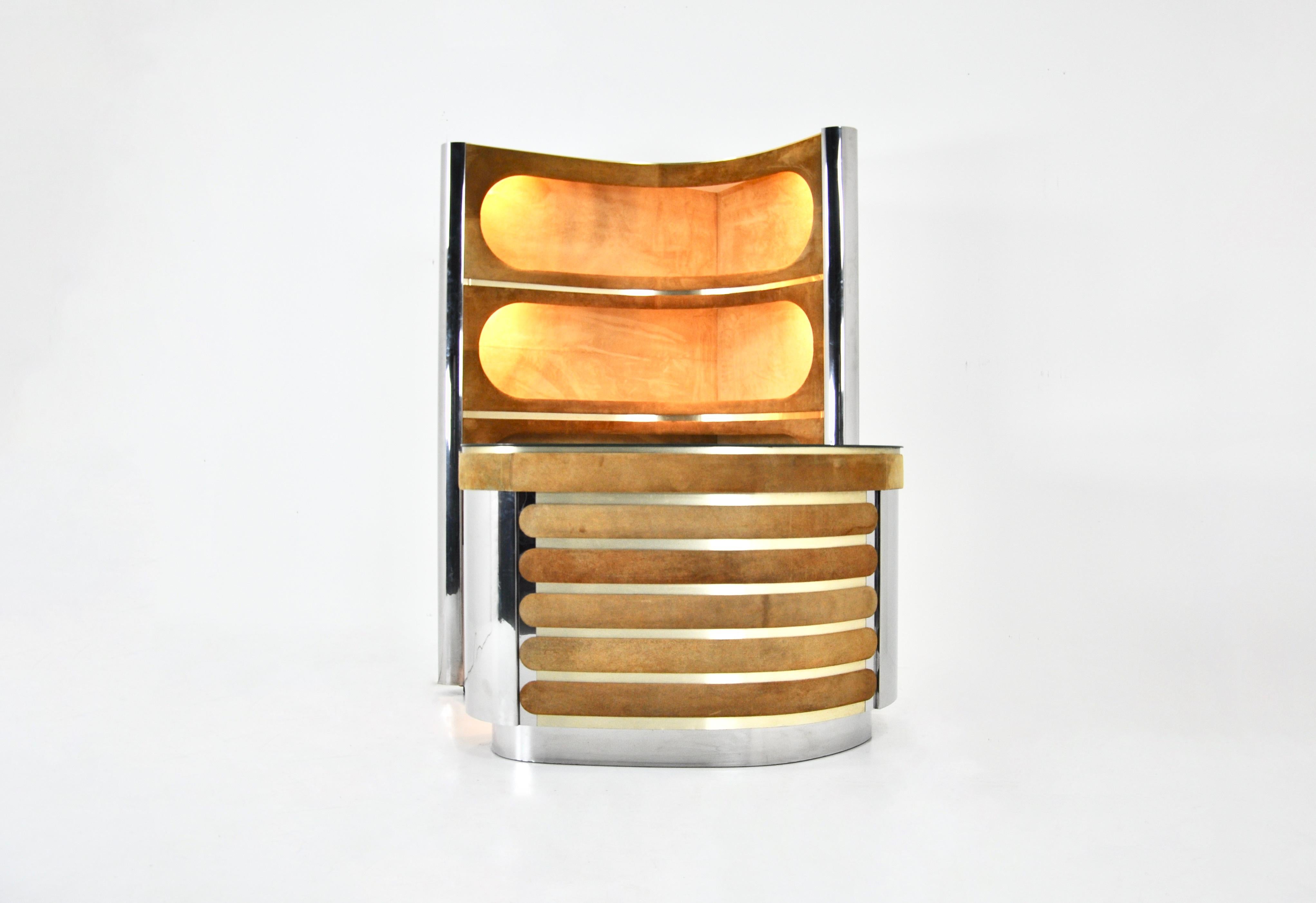 The set includes a cabinet with 3 illuminated shelves in suede, chrome metal and brass. It also includes a countertop in suede, chromed metal with a mirrored top, a new refrigerator and a showcase with a shelf. The floor is carpeted.
Shelf