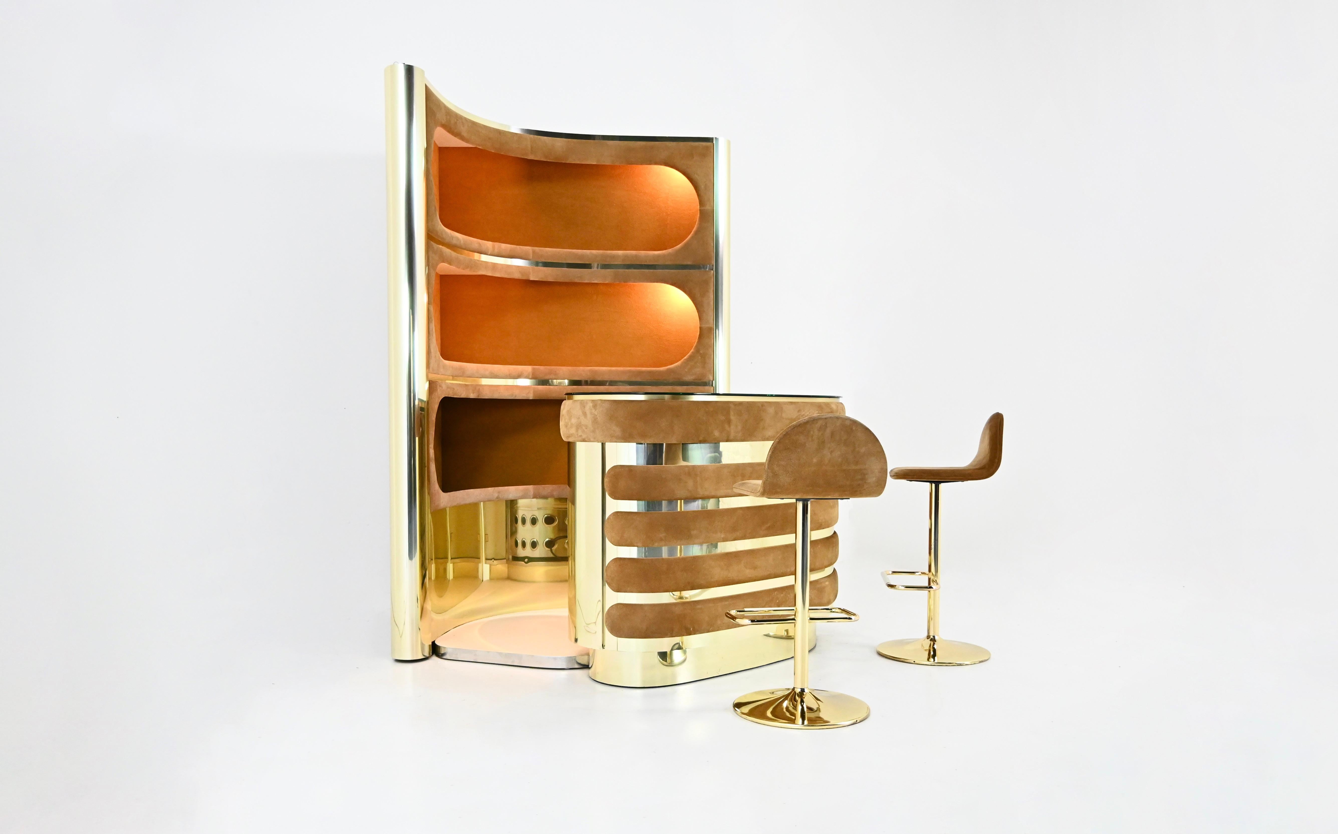 The set includes a cabinet with three illuminated shelves in suede and gold metal.  It also includes a counter in suede, gold metal, and a mirrored top, a refrigerator, and a glass display case with a shelf. The floor is carpeted. 
Dimensions of
