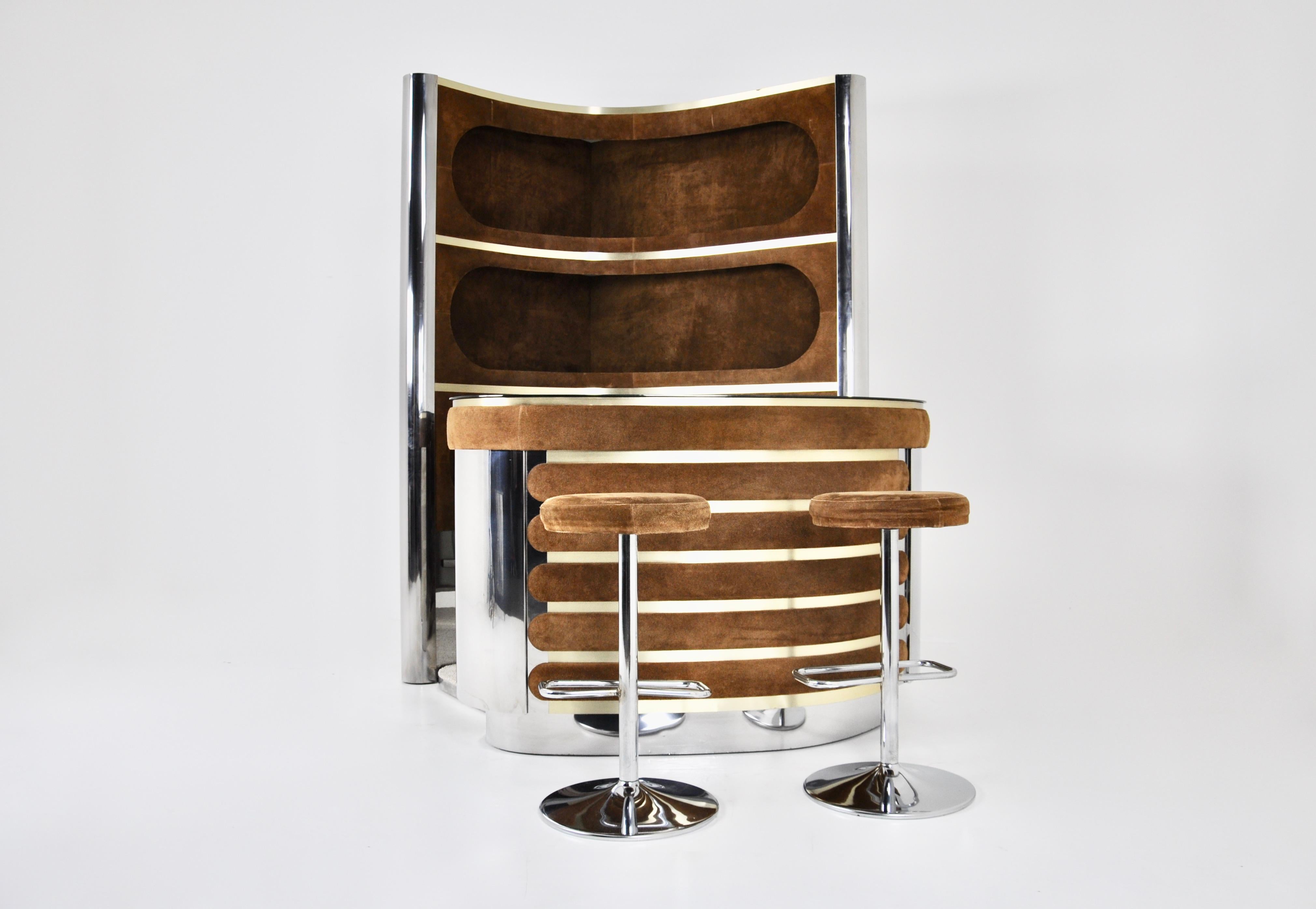 The set includes a cabinet with 3 illuminated shelves in suede, chromed metal and brass.  It also includes a counter in suede, chromed metal with a mirrored top, a fridge and a glass cabinet with a shelf. There is a carpeted floor. Height-adjustable