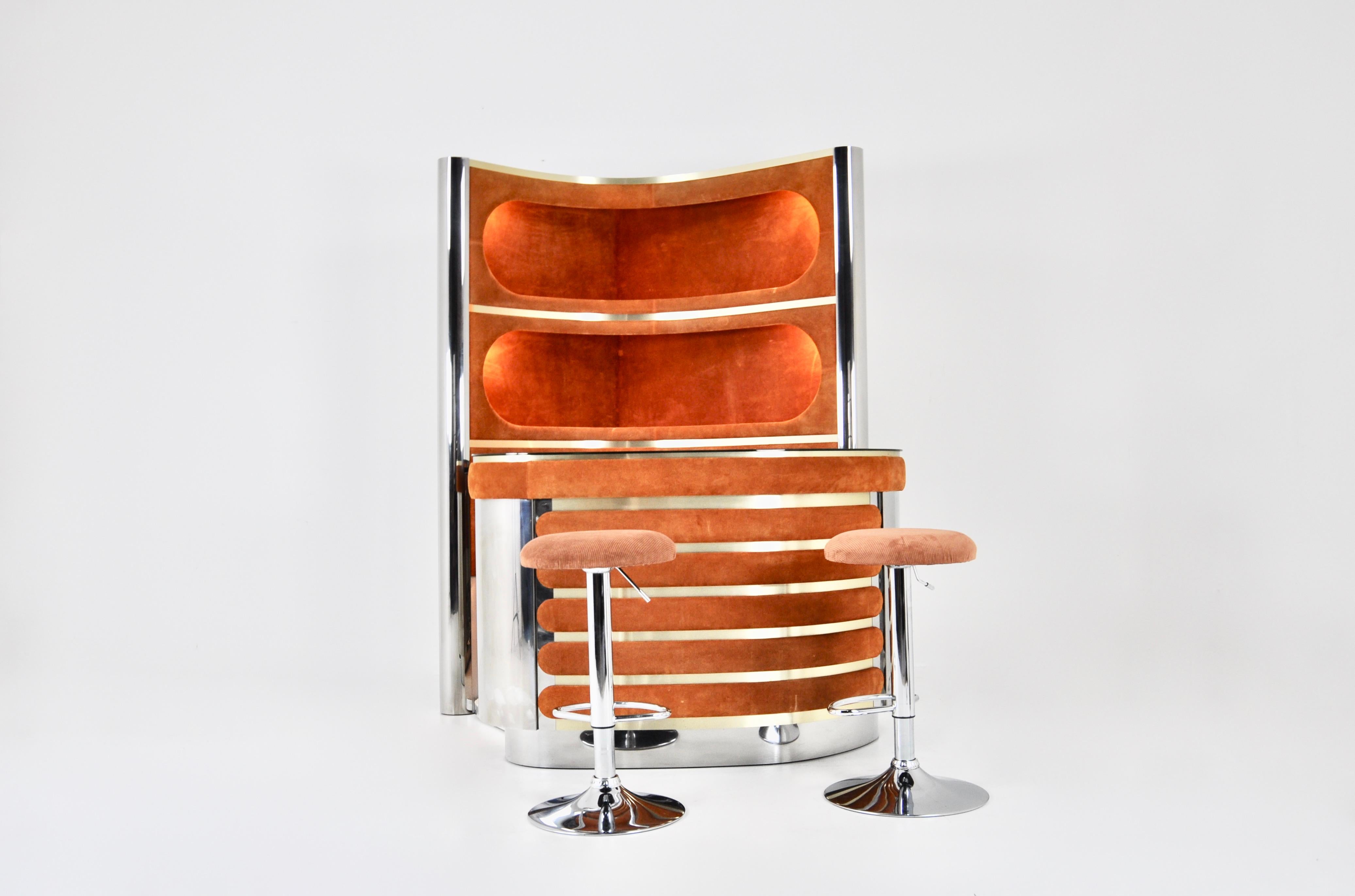 The set includes a cabinet with 3 illuminated shelves in suede, chromed metal and brass.  It also includes a counter in suede, chromed metal with a mirrored top, a fridge and a glass cabinet with a shelf. There is a carpeted floor. Height-adjustable