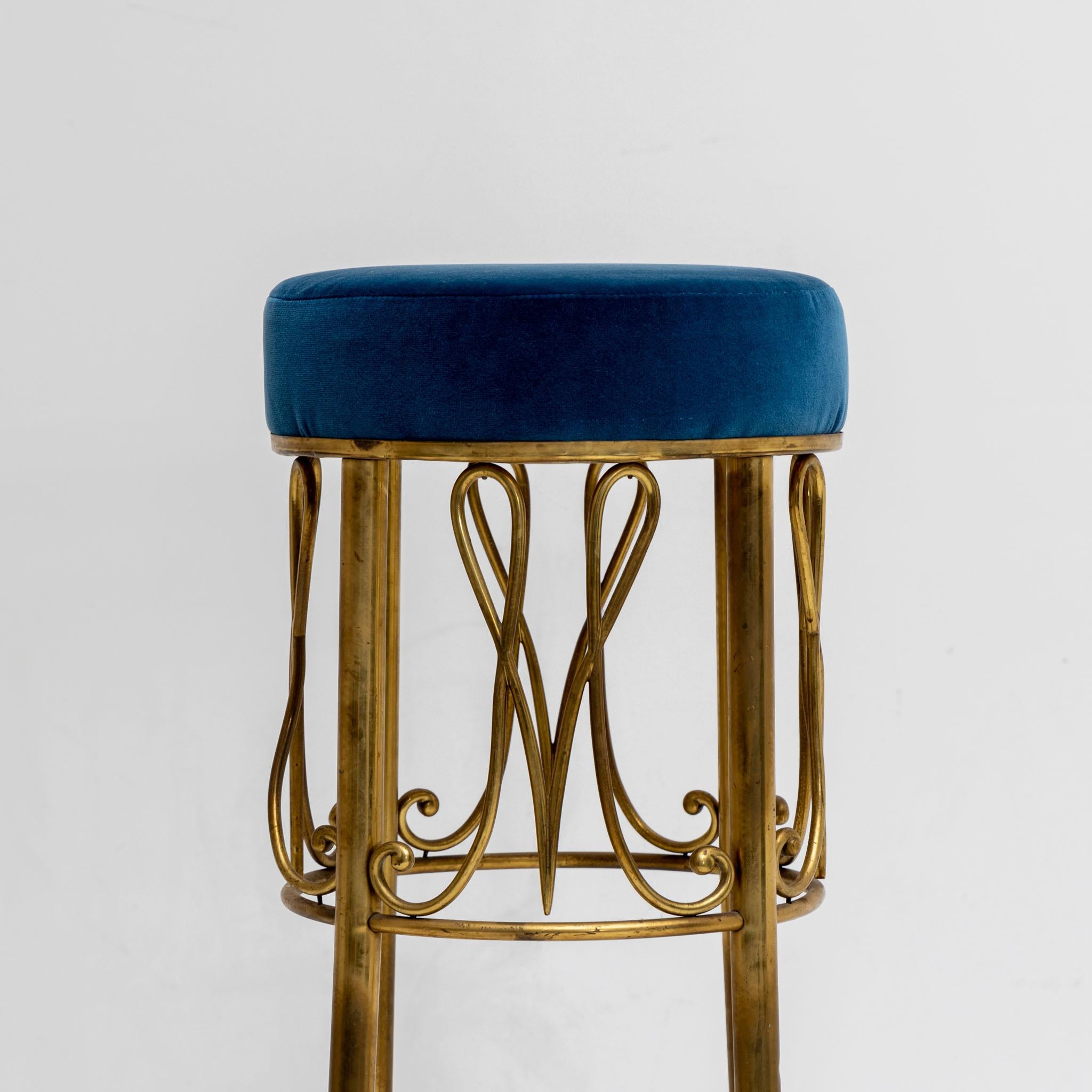 Upholstered bar stool with blue velvet cover and brass frame with M-shaped motifs.
