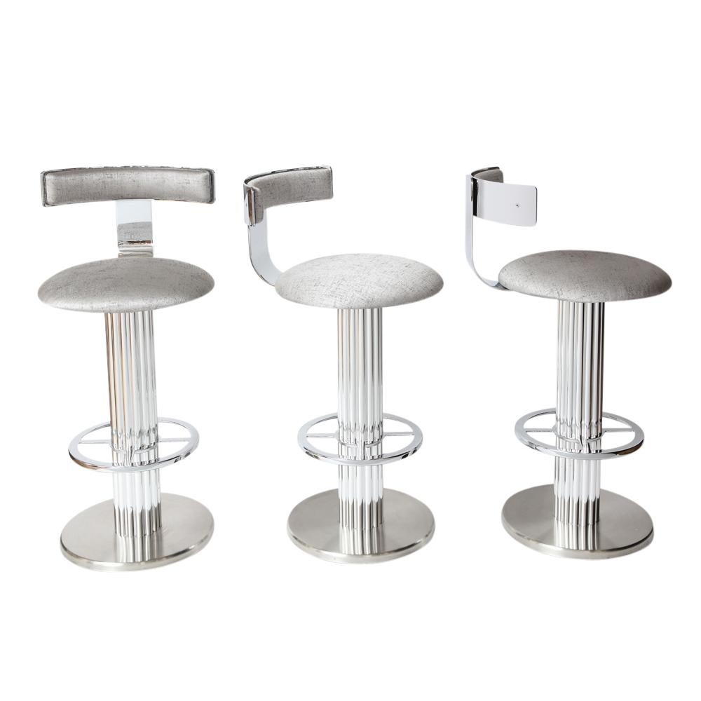 Bar stools by Designs for Leisure, chrome steel, swivel. Set of three heavy swivel barstools with high polished steel backrests and foot rests, polished aluminum reeded columns and brushed steel bases. Re-upholstered in a medium weight silver cotton