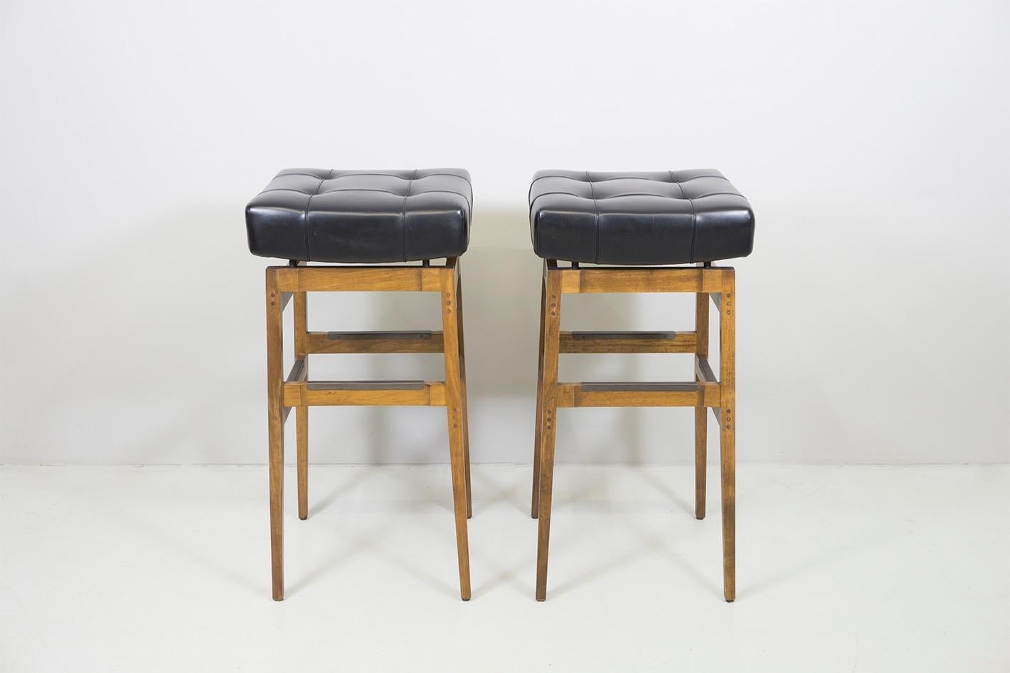A pair of bar stools with a construction solid walnut and black lacquered metal, upholstery and vinyl cover. With manufacturer label 'Cassina'.
Dimensions: H. 82cm 41 x 41cm.
Design: Gianfranco Frattini, 1958.
Manufacturer: Cassina, Italy.
 