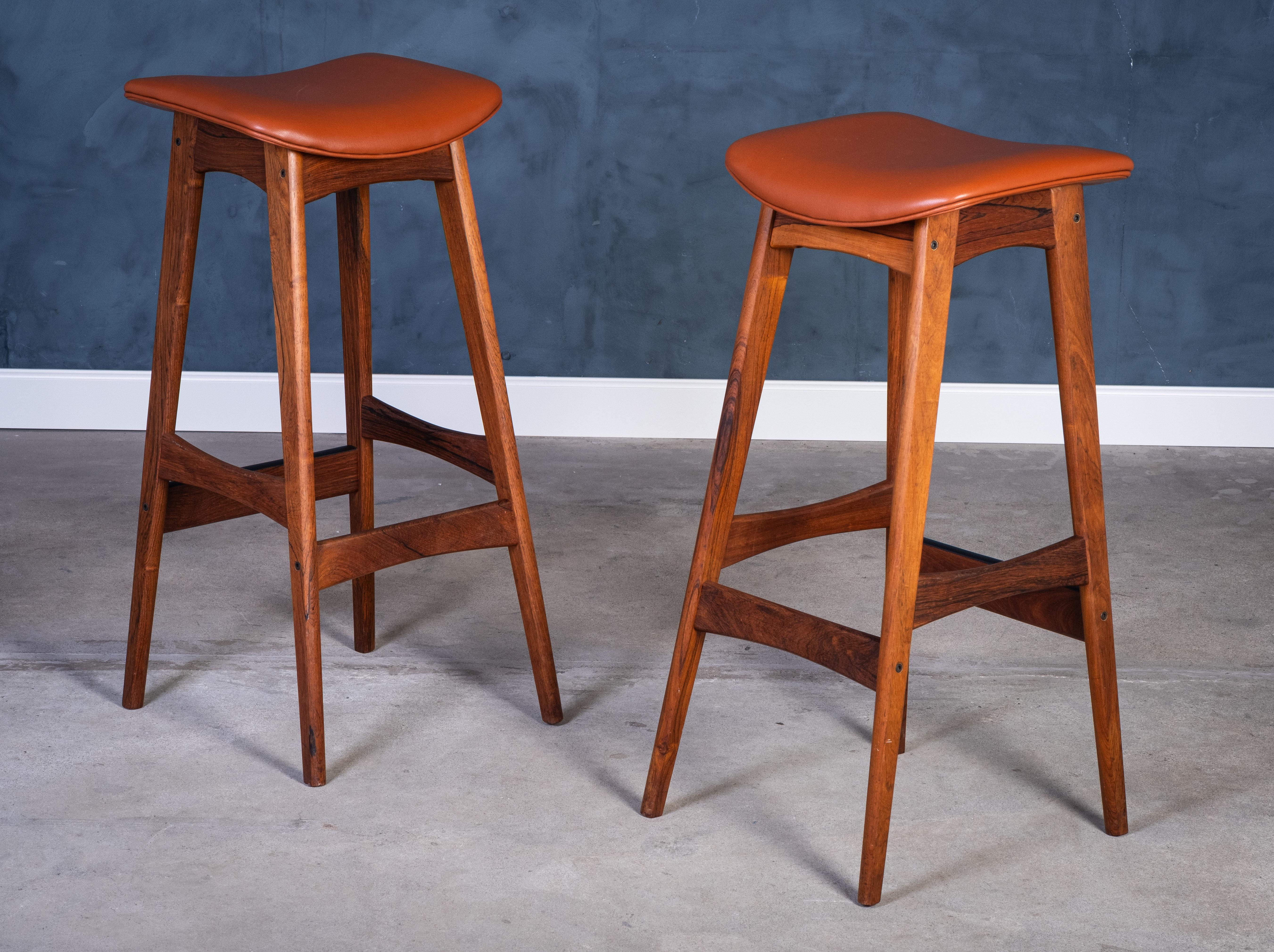 Stunning set of two bar stools designed by Erik Buch and produced by Dyrlund. Crafted from richly grained rosewood and upholstered in warm cognac leather, these stools embody the elegance and craftsmanship of classic Danish design.

The sculptural