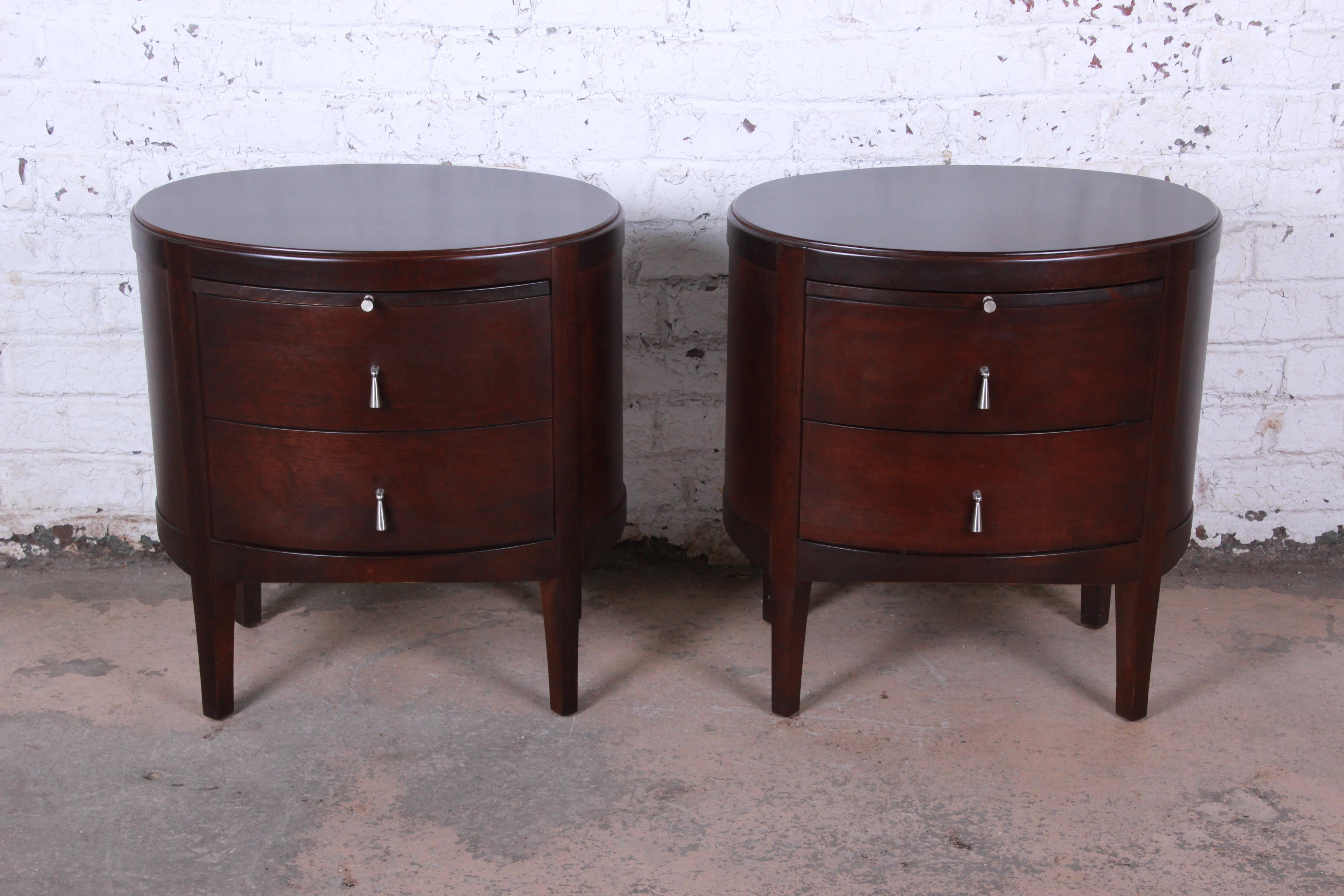 Offering a gorgeous pair of oval nightstands designed by Barbara Barry. The nightstands feature beautiful dark mahogany wood grain and nice contemporary design. They offer good storage, each with two deep drawers as well as a pull-out writing