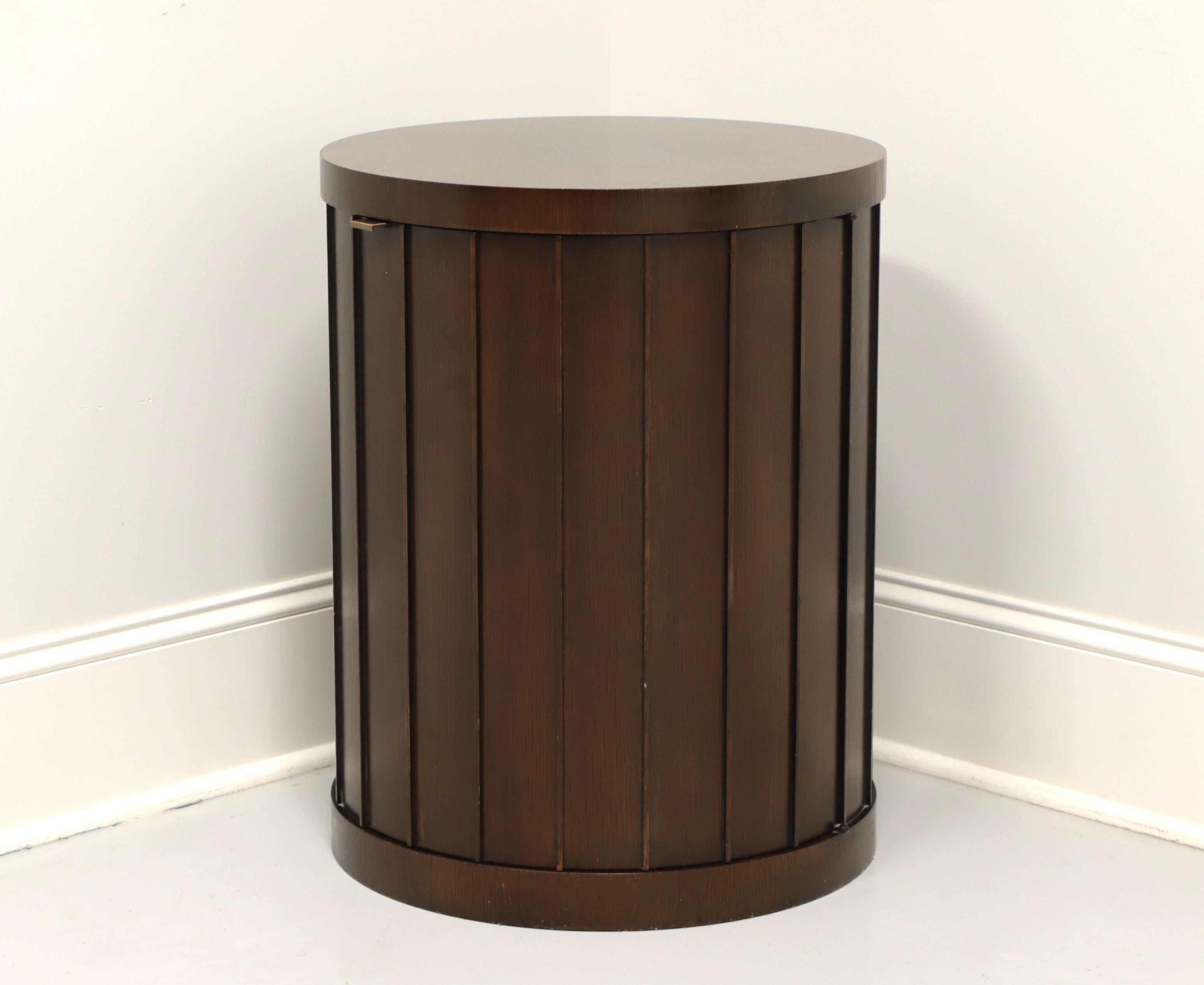 A Contemporary style round shaped cabinet accent table by Barbara Barry for Baker Furniture. Solid mahogany with a brass pull, inlaid top and architectural slats base. Features one hidden door revealing an ample interior storage area with one wood