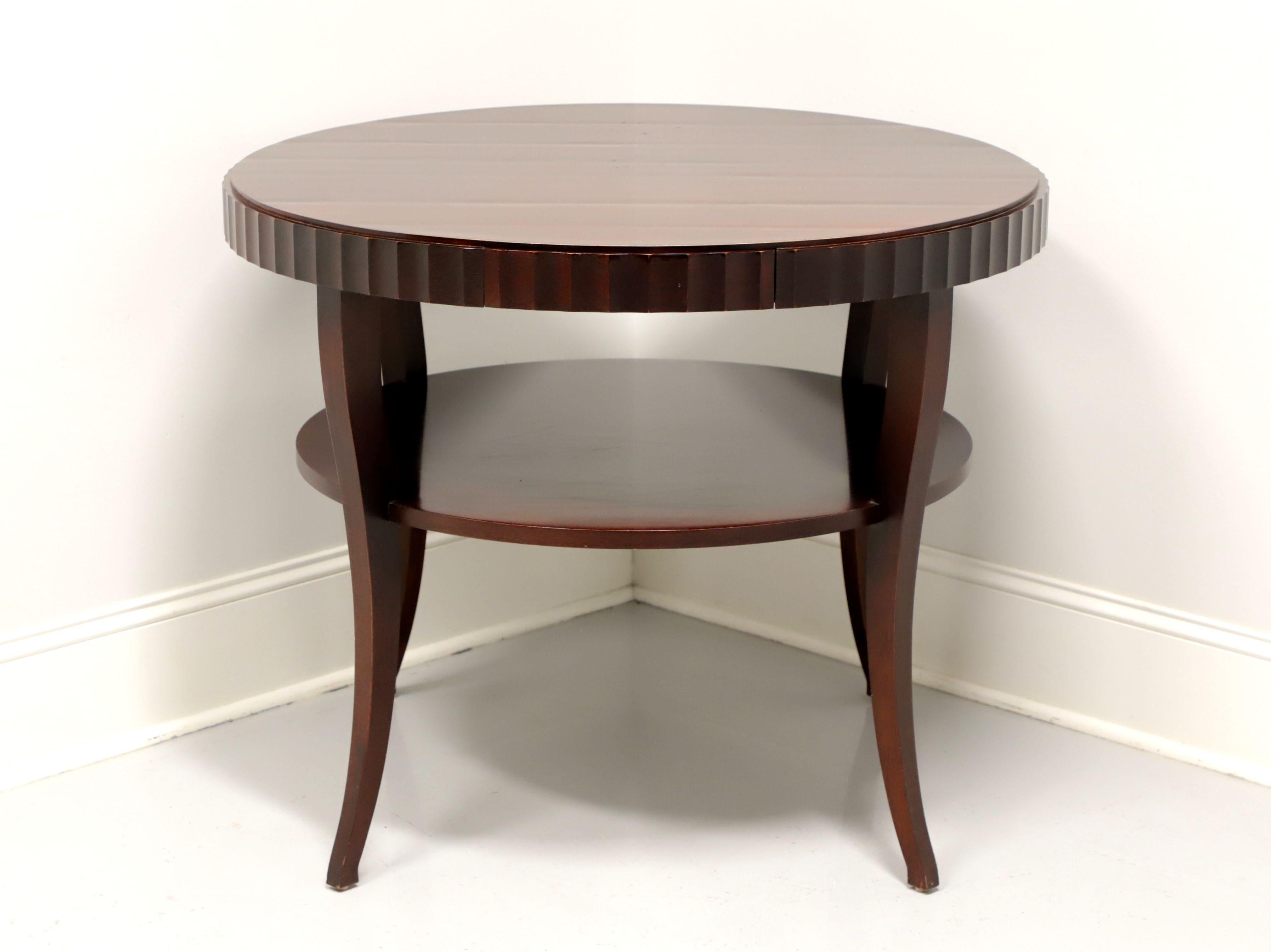 A Contemporary style round two-tier center accent table by Barbara Barry for Baker Furniture. Solid mahogany, with one hidden drawer in the scalloped apron, an undertier shelf and tapered saber legs. Made in the USA, in the early 21st