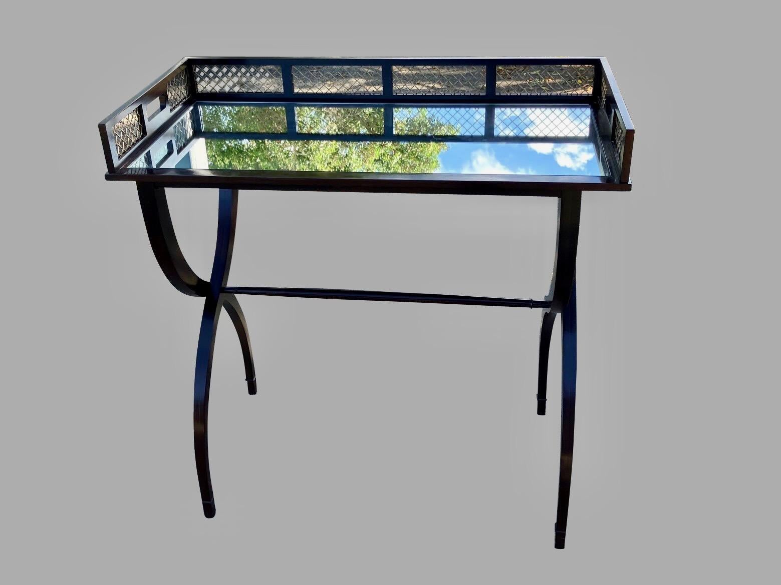 A stylish ebonized hardwood bar or drinks table designed by Barbara Barry and manufactured by Baker. The removable mirrored tray top has 2 side carry handles and is fitted with an antiqued brass mesh gallery. The tray rests on an attractive curved