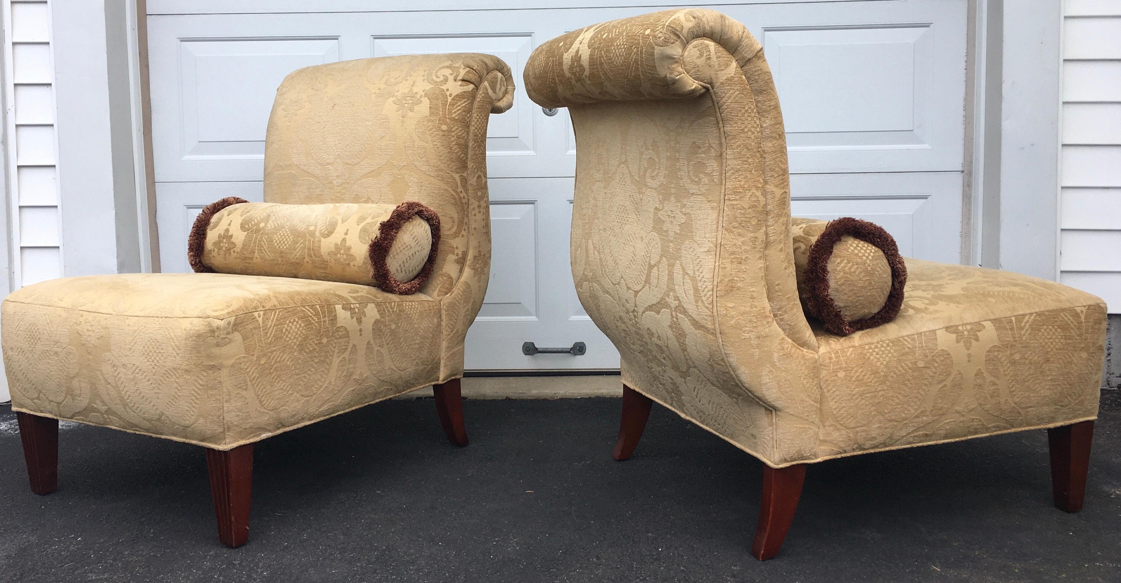 Pair of 1940s-inspired roll-back upholstered slipper lounge chairs by Barbara Barry for Baker Furniture. Sculptural curved frames feature heavy weight gold damask fabric with coordinating brush fringe trimmed bolster pillows and fluted front legs.  