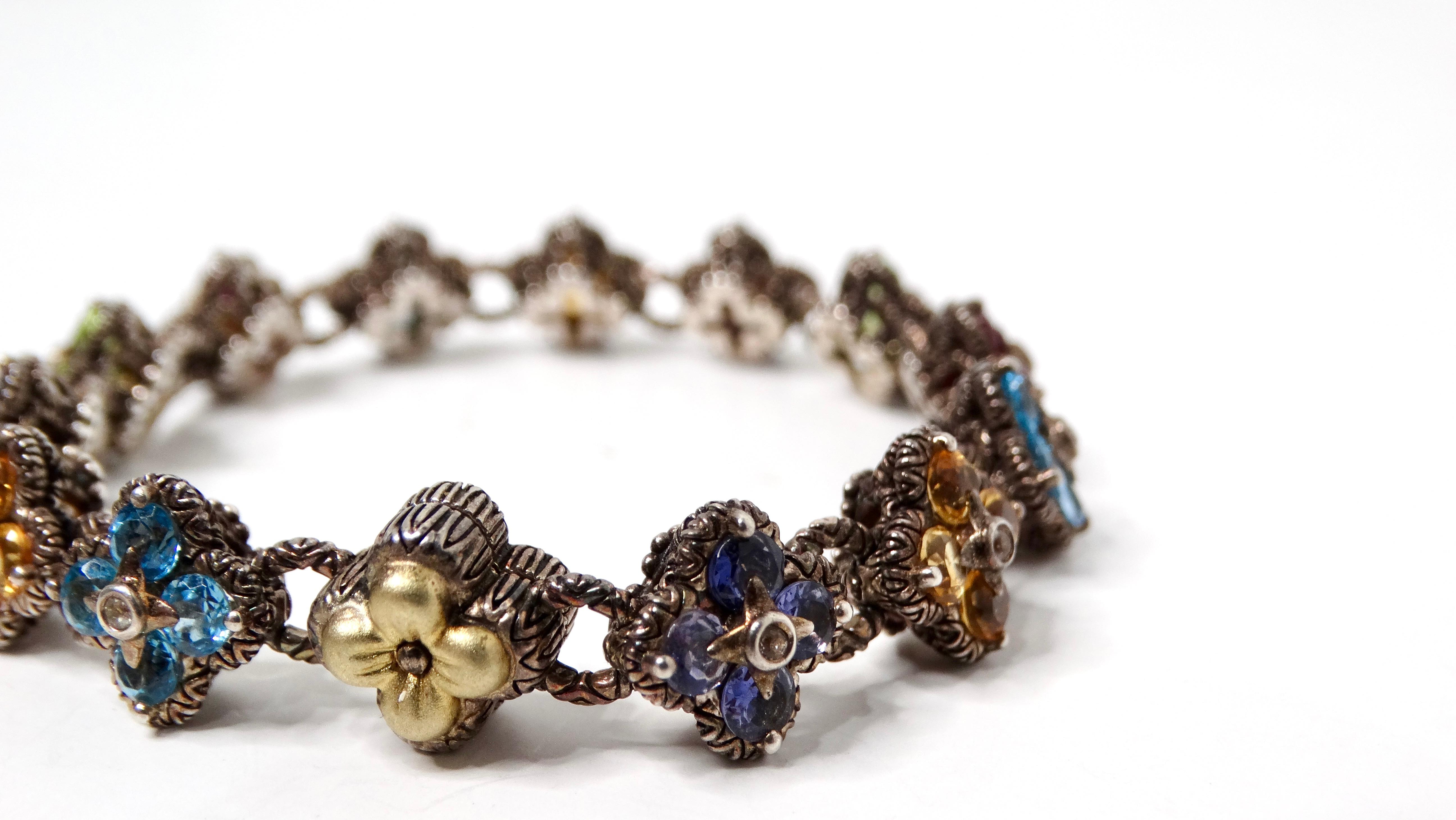 The Barbara Bixby Sterling Silver & 18k Gemstone Flower Bracelet is a stunning fusion of artistry and luxury. This captivating piece features a central 18k gold flower, elegantly juxtaposed against an array of colorful gemstone flowers crafted from