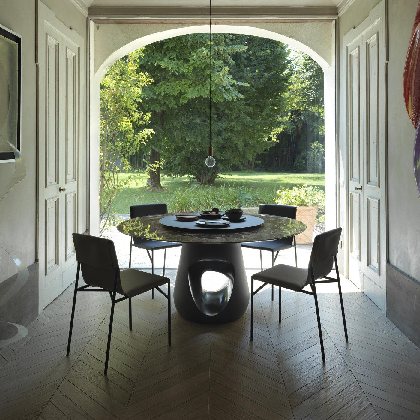 An oval or round top crafted of Emperador dark marble boasting its natural shapes and captivating hues is distinguishing element of this dining table designed by Roberto Zamberlan. A tribute to English sculptor Jocelyn Barbara Hepworth (1903-1975)