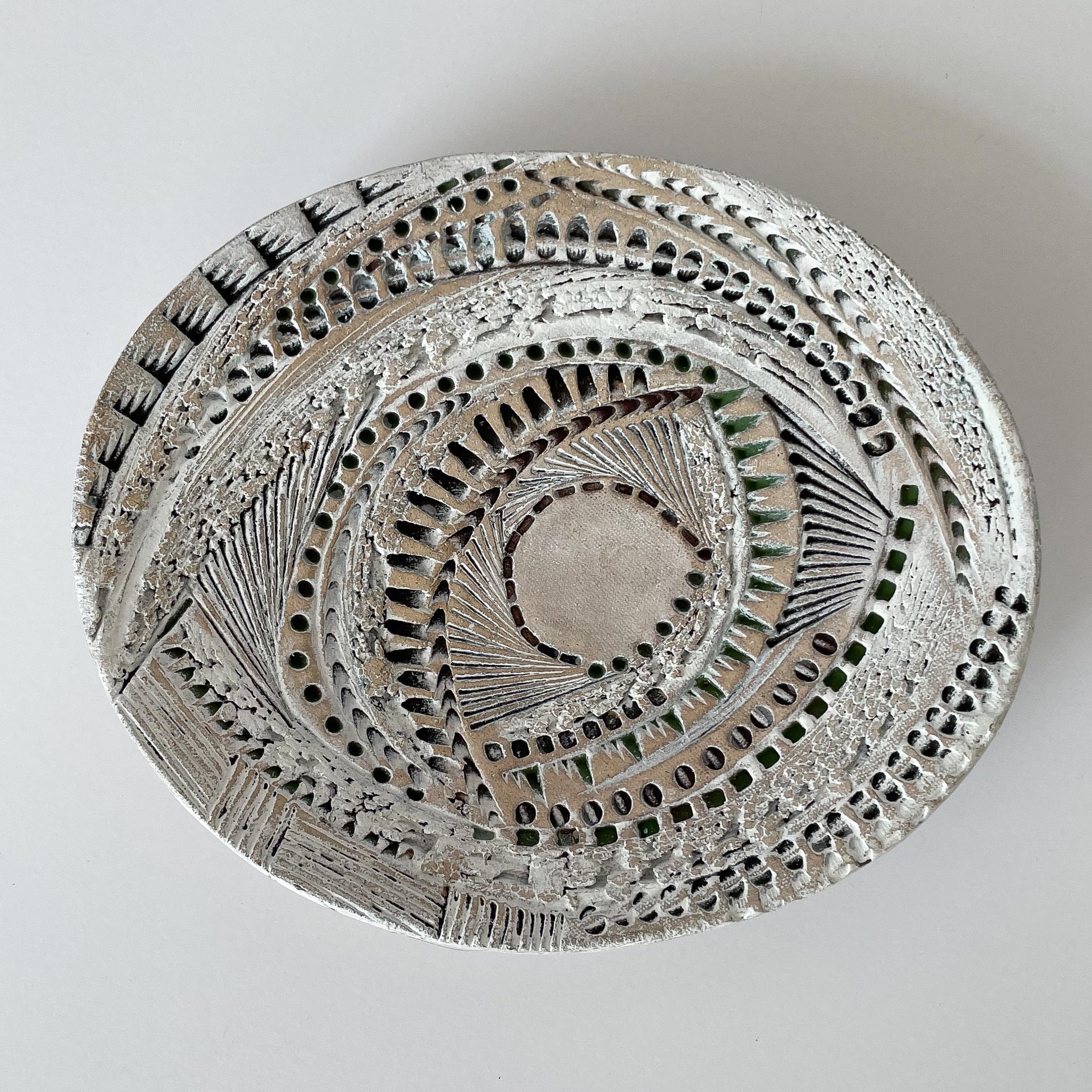 A studio pottery decorative footed dish by Barbara Haring, circa late 20th century. This ceramic dish features an intricate incised textured design. An abstract feather design and fishnet back. Glazed in white, green and black. Hints of the natural