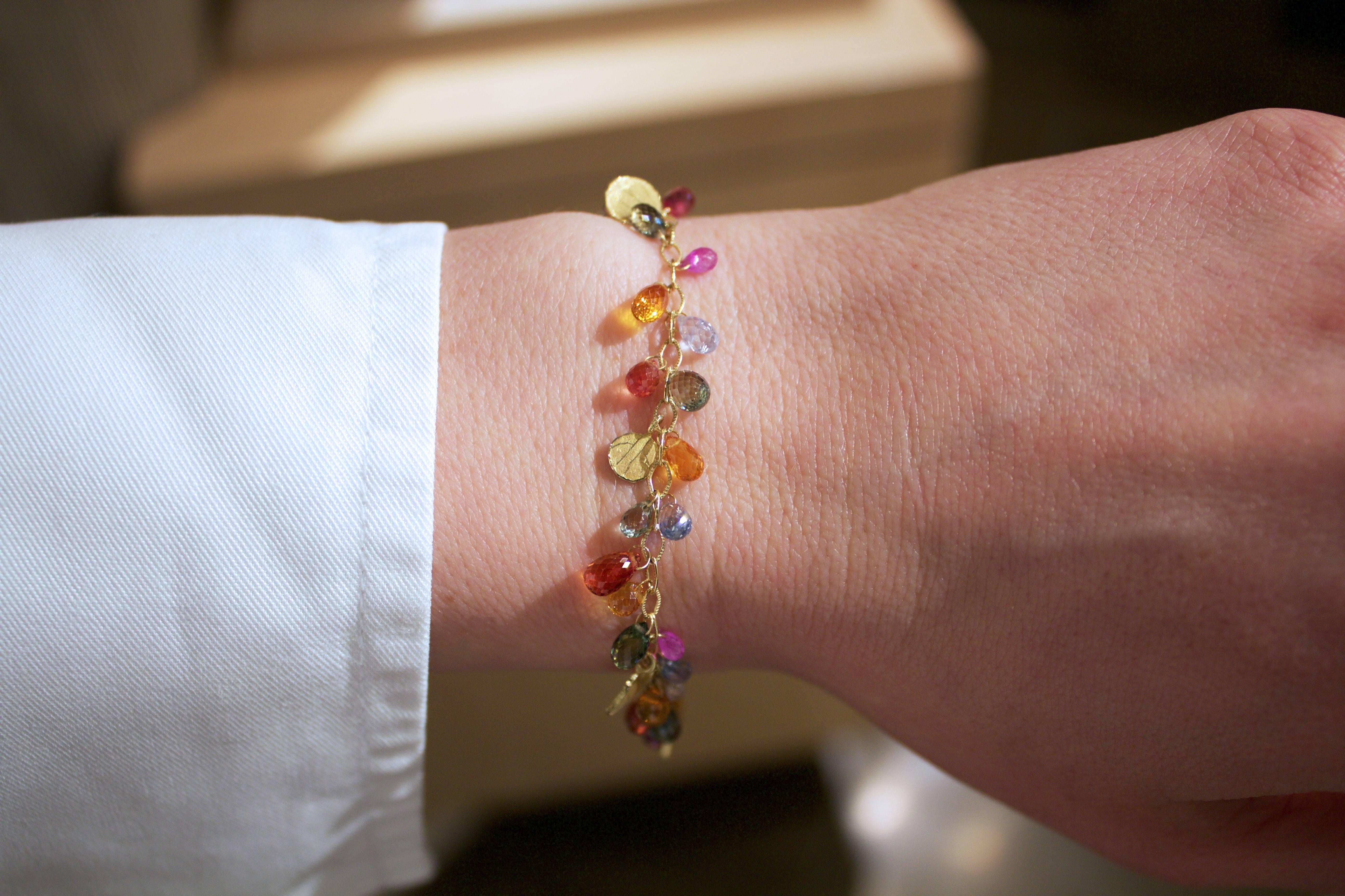 Petal Drop Bracelet handcrafted by award-winning jewelry artist Barbara Heinrich in matte-finished 18k yellow gold featuring an assortment of beautifully-faceted, vivid, multicolored sapphire briolettes accented with five signature petal spacers and