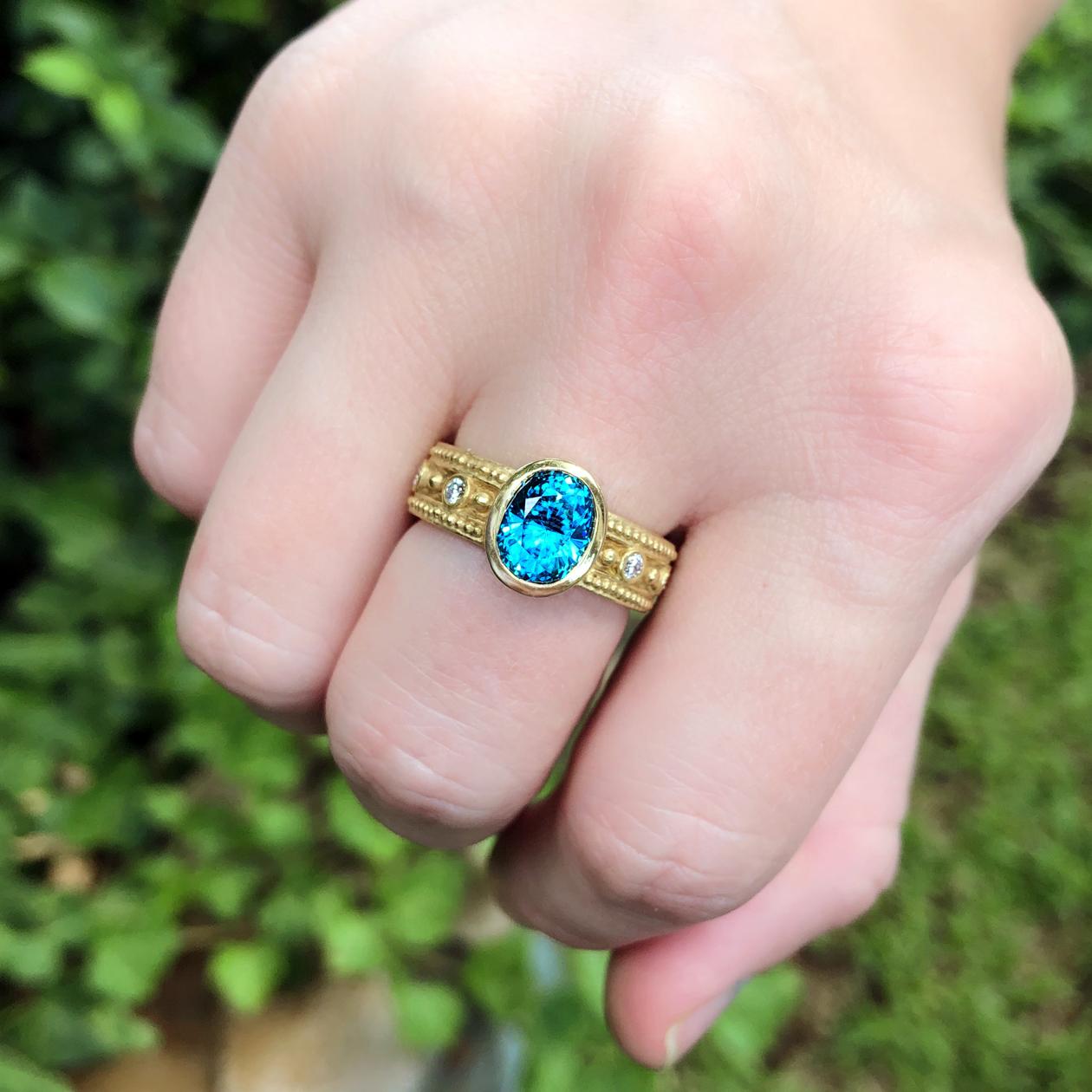 Granulated Rim Ring handcrafted by award winning jewelry maker Barbara Heinrich in her signature matte-finished 18k yellow gold featuring a dazzling natural 3.02 carat faceted oval blue zircon and accented with 0.31 total carats of round