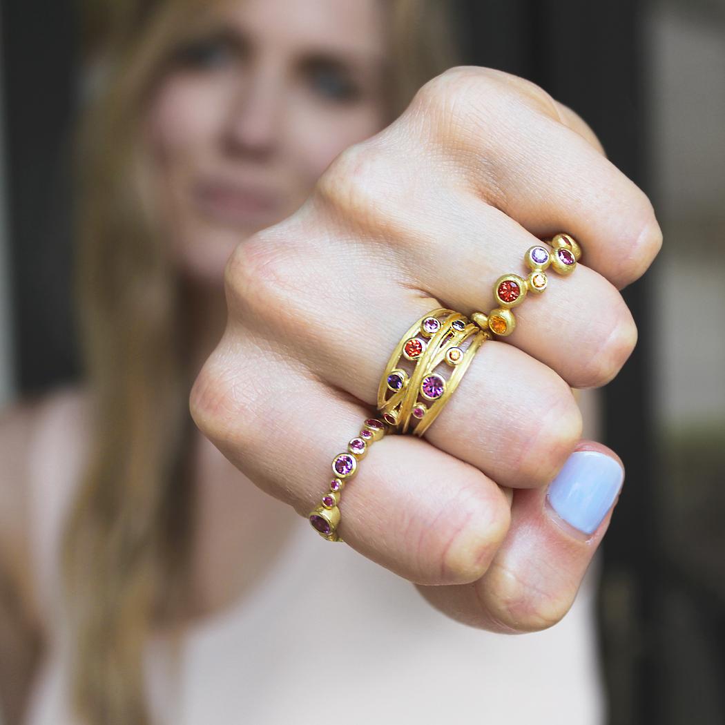Random Bubble Band Ring handcrafted by award winning jewelry artist Barbara Heinrich in matte-finished 18k yellow gold showcasing 1.83 total carats of multicolored round sapphires in vibrant oranges, yellows, reds, purples, pinks, violets, and more.