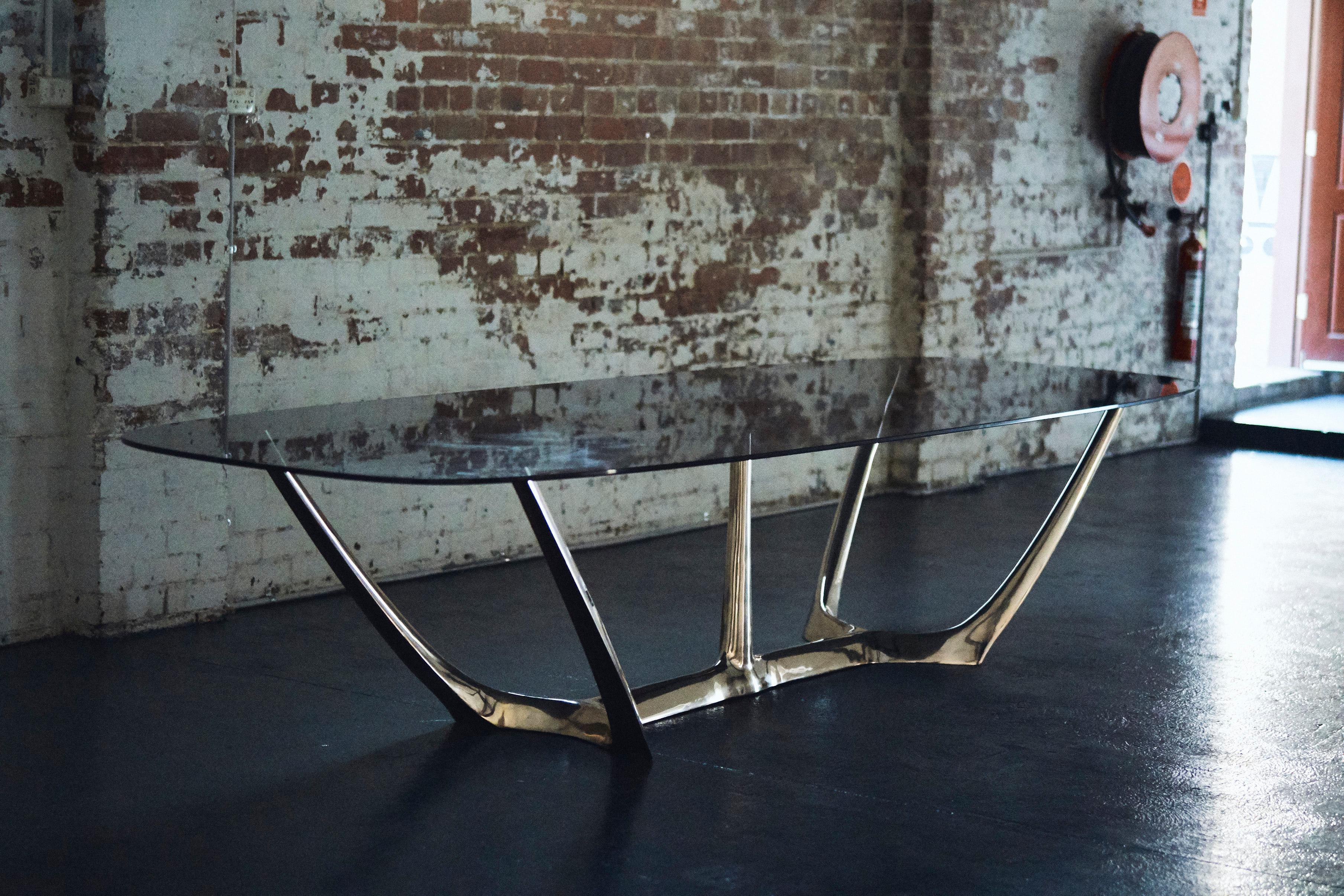 Der von Daniel BARBERA entworfene Esstisch besteht aus einer skulpturalen Form aus Bronze, die mit grau getöntem Hartglas kombiniert ist. Der große Esstisch ist die Krönung einer über zehnjährigen Arbeit mit Bronze. Inspiriert von Organismen und