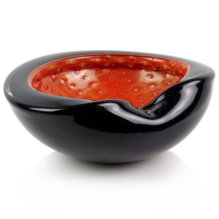 Beautiful vintage Murano hand blown black over persimmon orange and gold flecks Italian art glass decorative bowl. Documented to designer Alfredo Barbini. It has a thick folded over rim. The inside also has controlled bubbles, which grab the gold