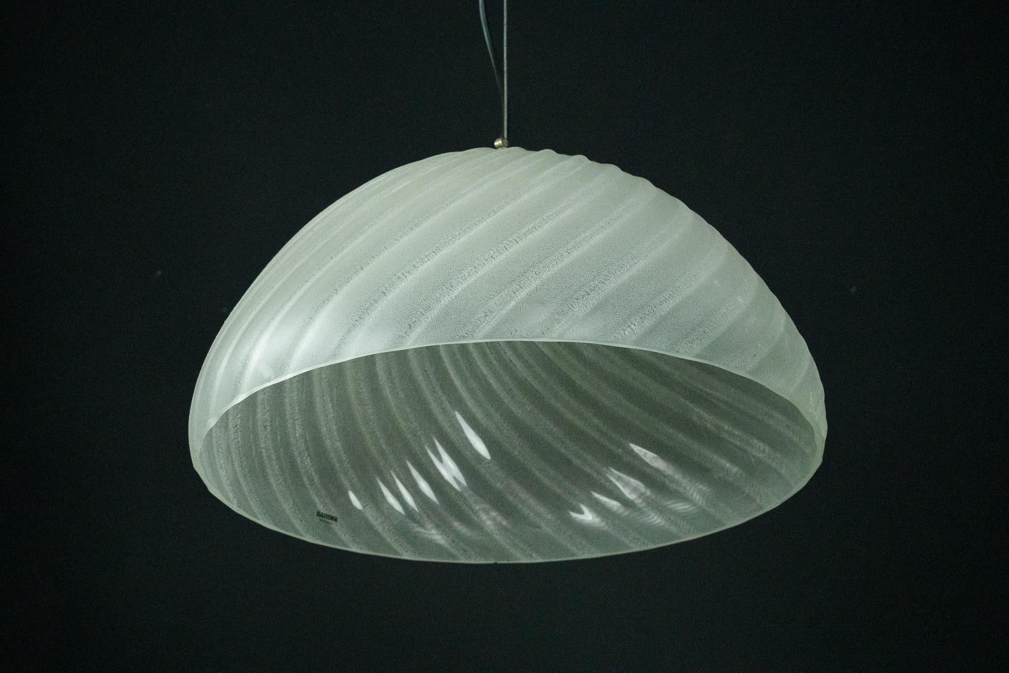 This elegant pendant lamp was crafted by Barbini in Murano, Italy, during the early 1980s. Made from high-quality Murano glass and brass details, its design showcases a sophisticated ribbed texture with a translucent finish, embodying the timeless