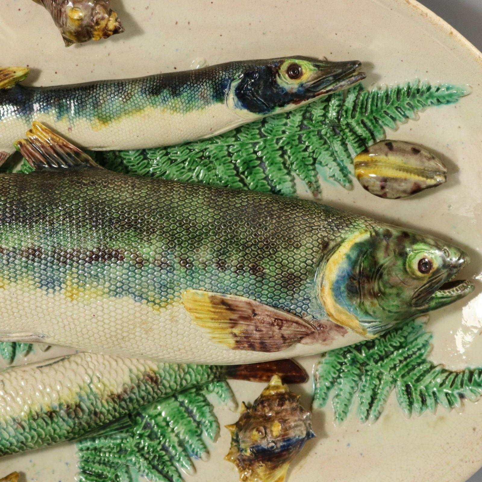 Plat mural Barbizet en majolique française de Palissy qui présente divers poissons et coquillages superposés sur un lit de feuilles de fougère. Coloration : le blanc, le vert et le bleu sont prédominants.