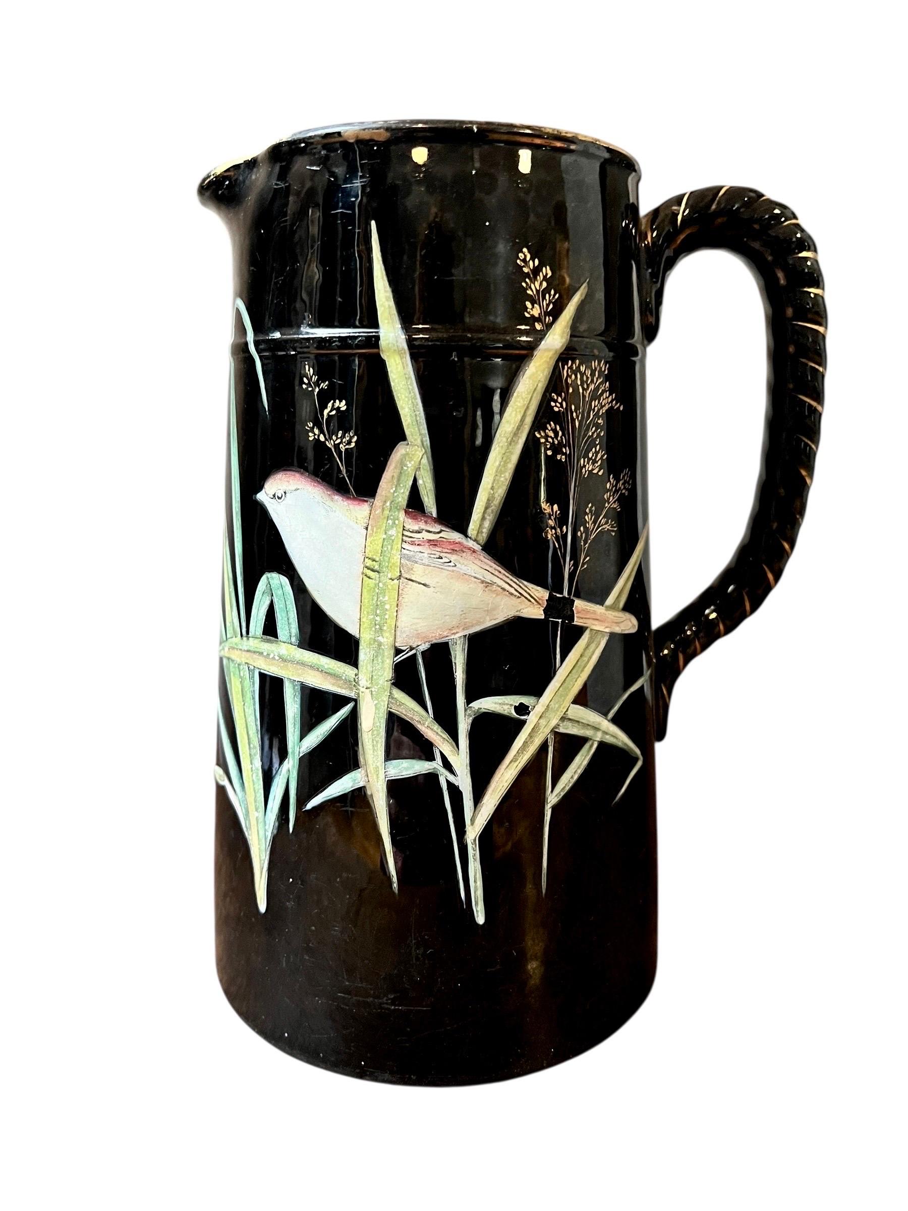 Beautiful cylindrical pitcher with a glossy black base, decorated with a bird among reeds painted in polychrome slip, with small grasses highlighted in gold. Twisted 