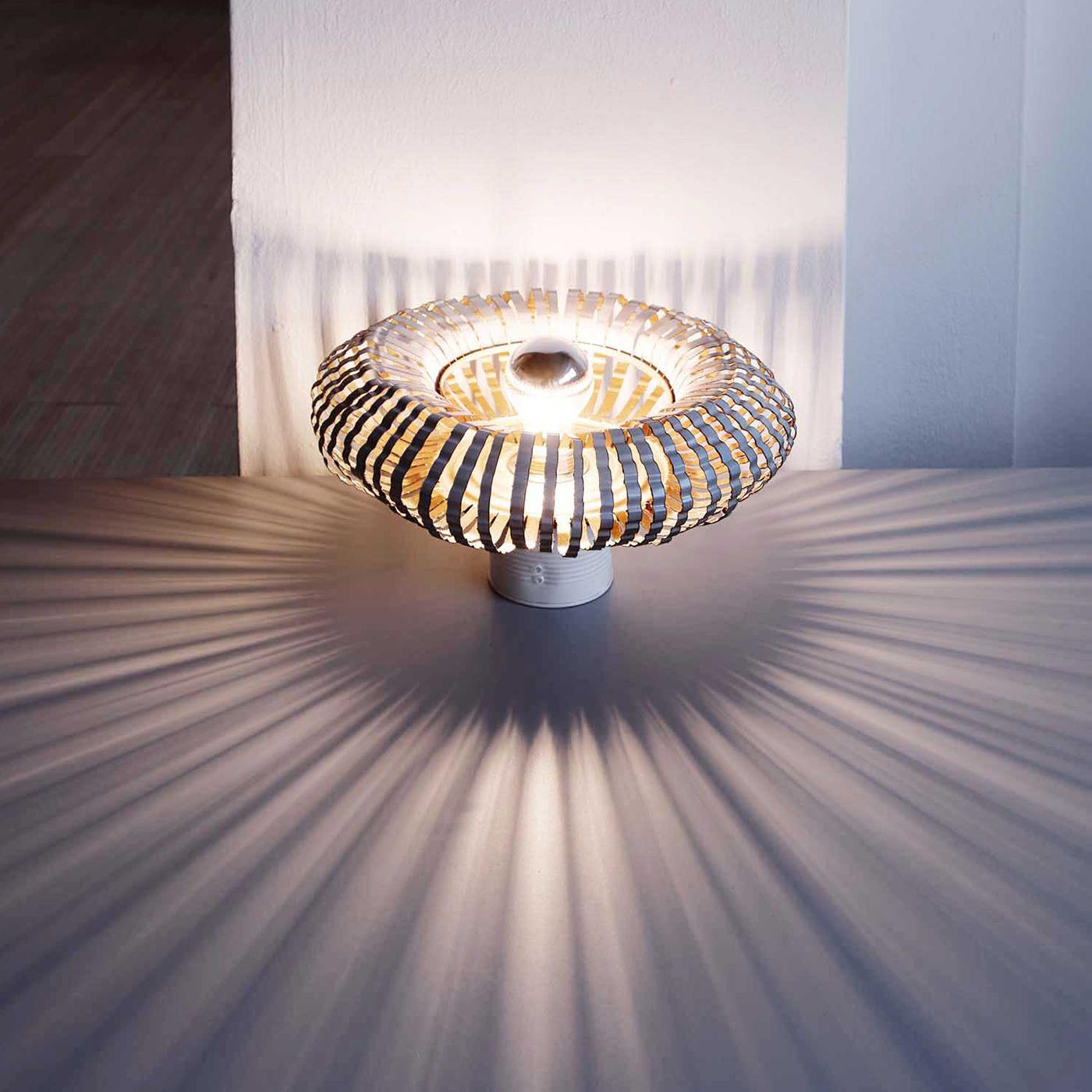 La lampada da tavolo Barby è l'esatto opposto della sua iconica omonima e ci seduce con le sue linee morbide e la sua armoniosa rotondità. Realizzata con oggetti metallici riciclati e riutilizzati, come barattoli di cibo e di vernice, questa