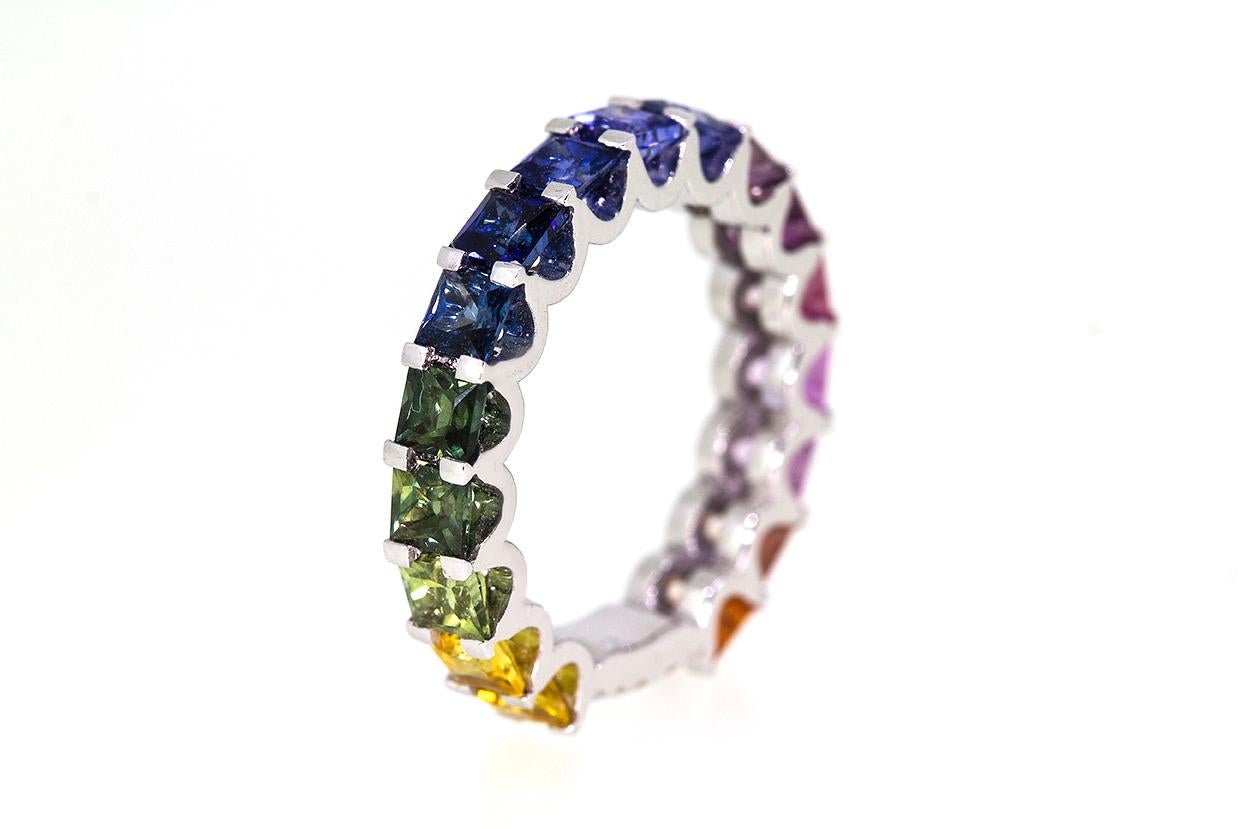 The Barcelona Rainbow Princess Cut Sapphire 18 Carat White Gold Eternity Band Ring is a graduated rainbow on your hand measuring approximately 3.3.6mm in width. The ring features one row of 17 x scalloped claw settings of a graduating rainbow effect