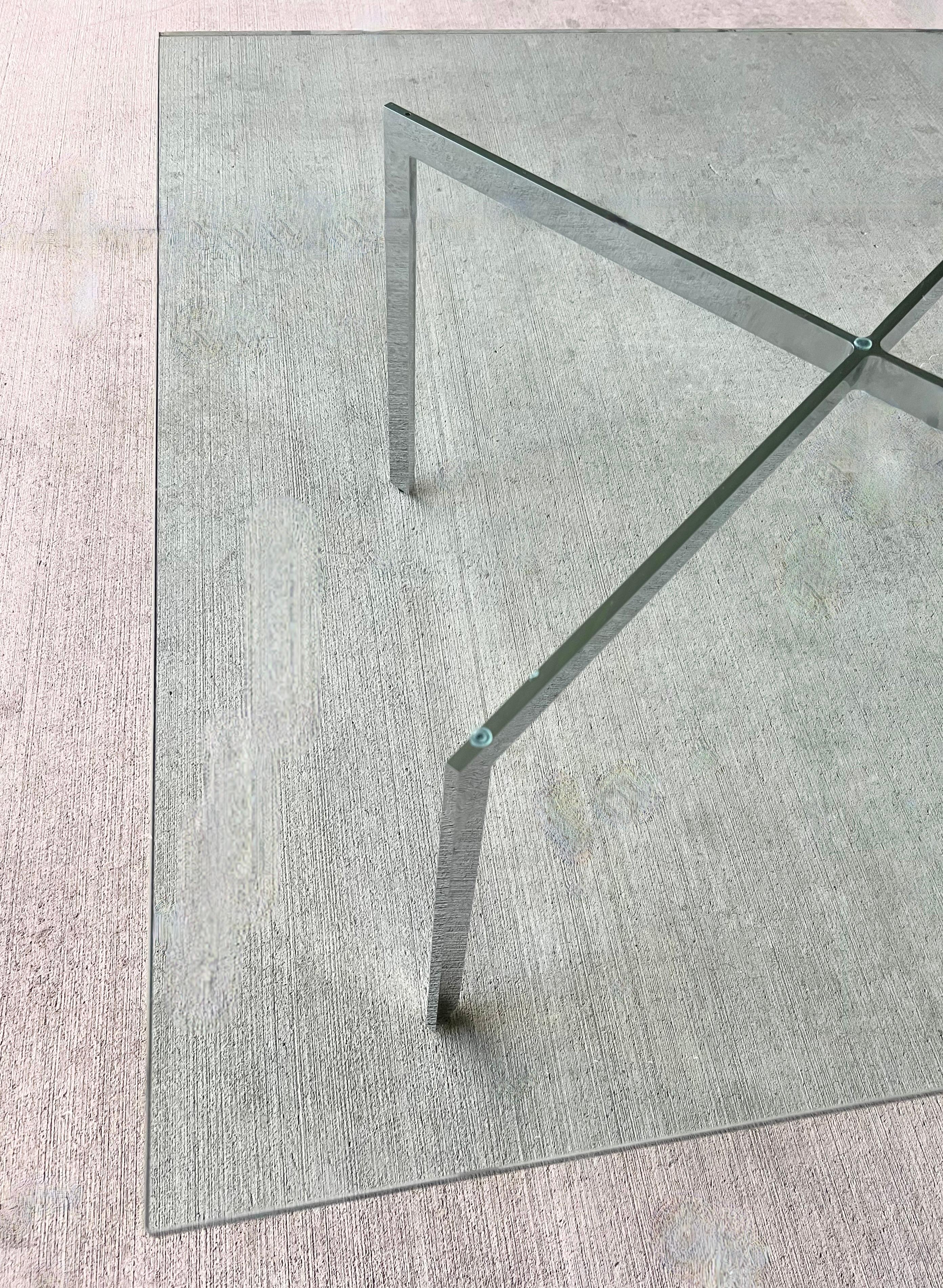 Iconic Barcelona Modernist X-Base Coffee Table from Mies van der Rohe.  Made in the 1970’s.  Solid stainless steel frame with the original 1/2” thick heavy glass top with rounded corners and a slight green tint. The silver frame is in excellent