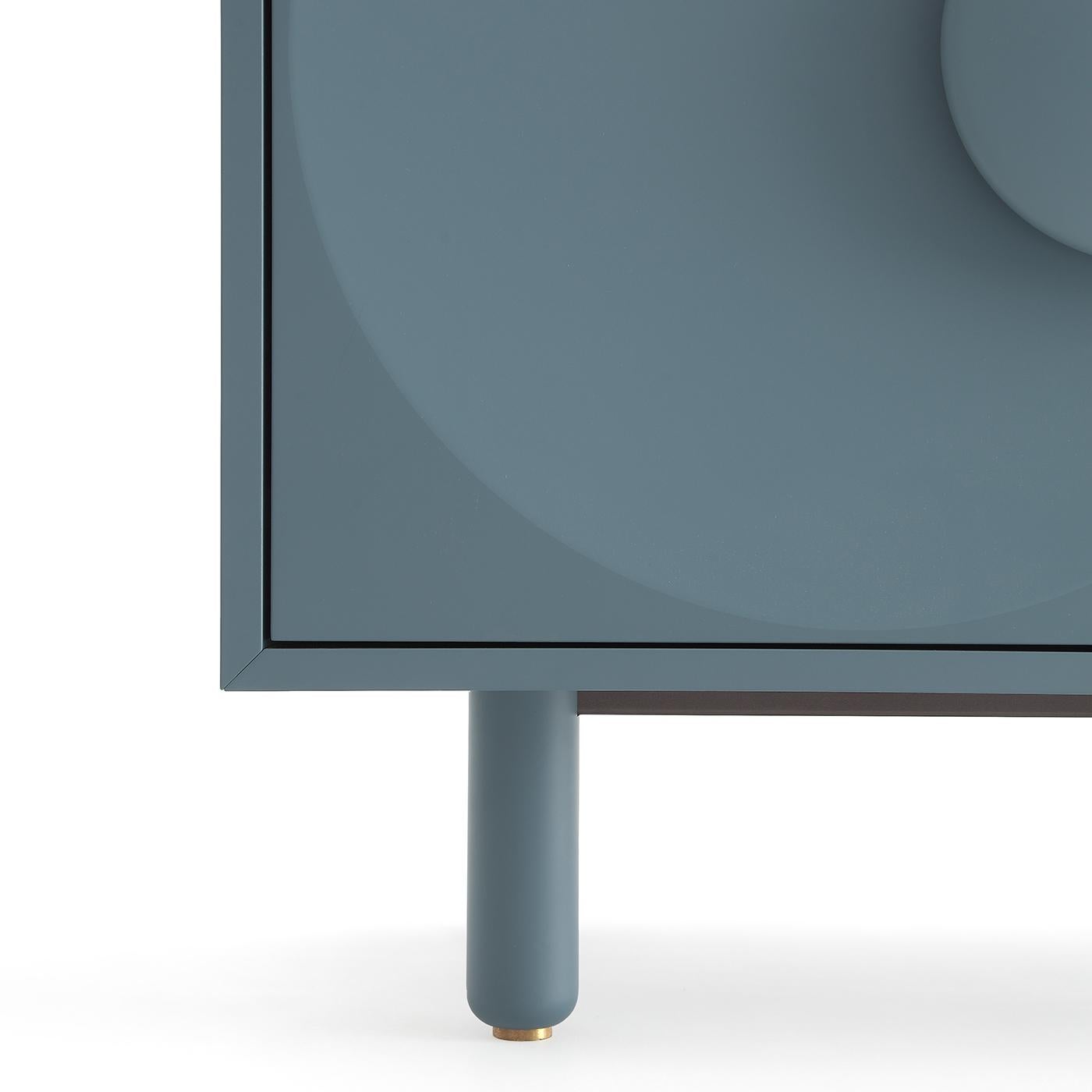 Questa credenza compatta presenta maniglie a forma di bottone che emergono da leggere depressioni, dettagli che celebrano la tendenza francese degli anni '20 a concedersi ai bottoni. Per la struttura in MDF è stata scelta un'elegante tonalità di blu